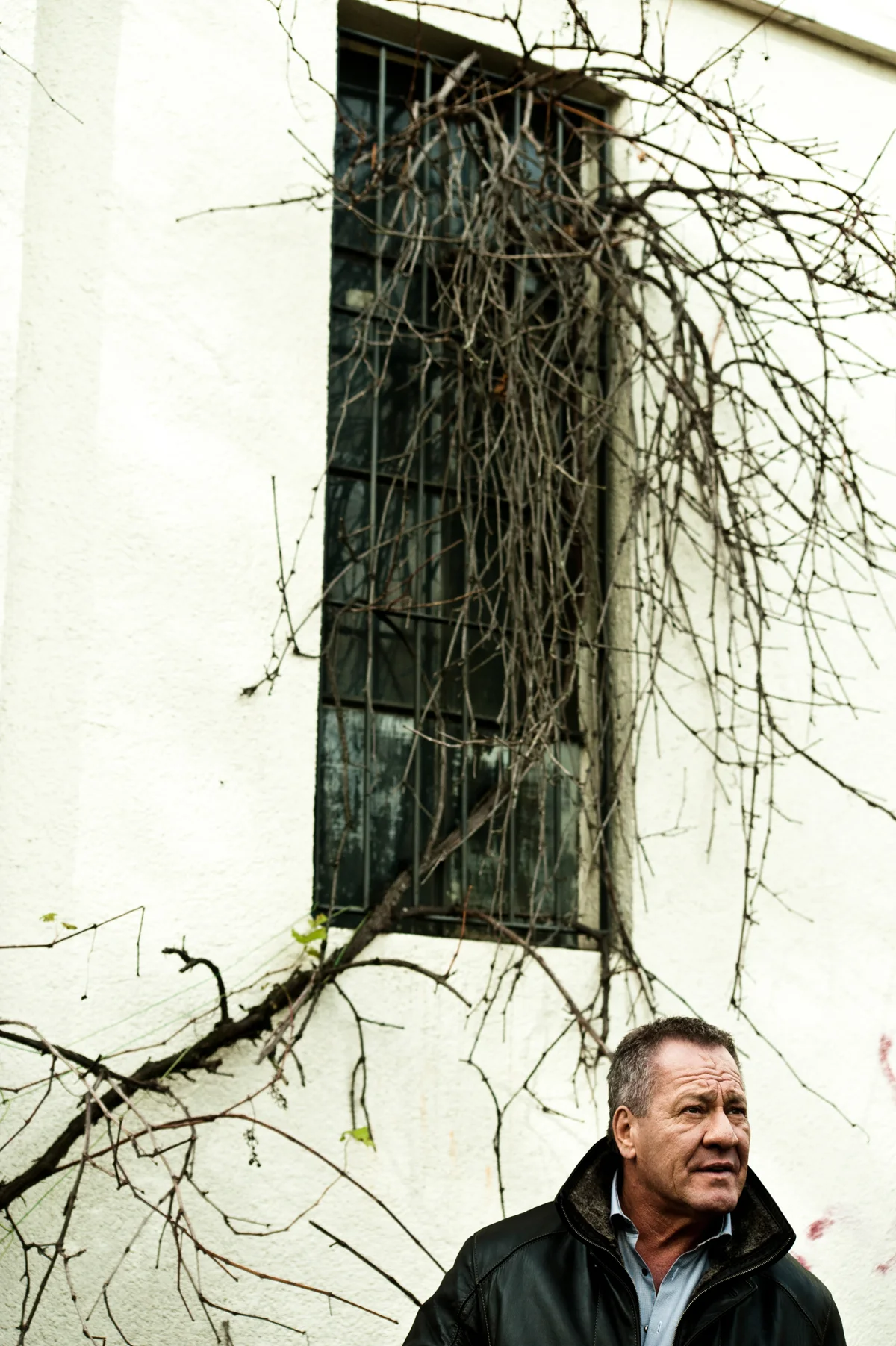 Hugo Bachmaier below a barred window with bare branches — Hugo Bachmaier, portrait photography by Janina Laszlo