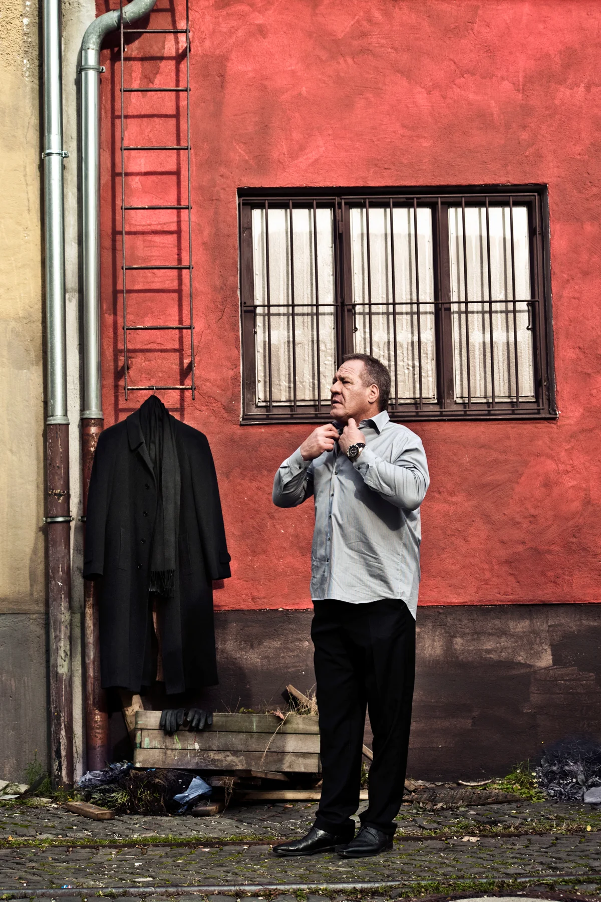 Hugo Bachmaier in front of a red wall with a coat hanging beside him — Hugo Bachmaier, portrait photography by Janina Laszlo