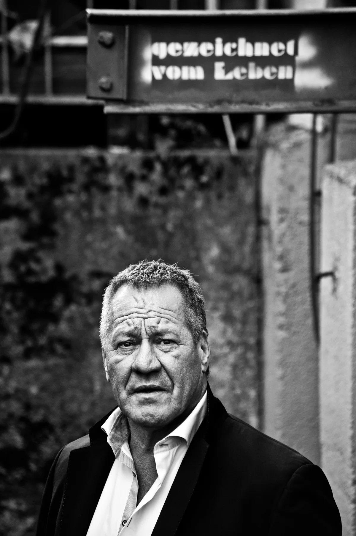 Black-and-white portrait of Hugo Bachmaier below a shop sign — Hugo Bachmaier, portrait photography by Janina Laszlo