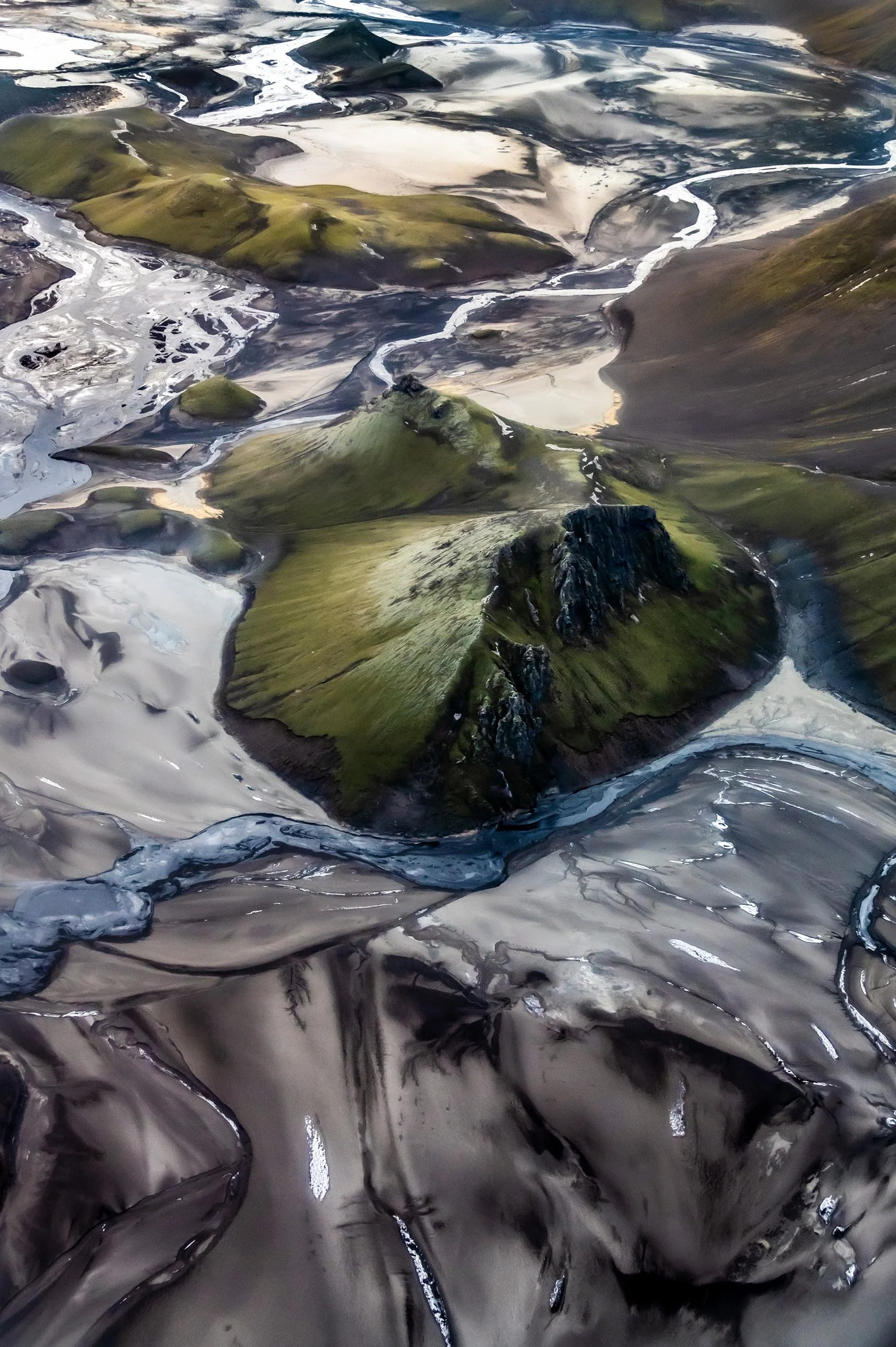 Green moss-covered hill surrounded by black lava sand, aerial photograph of Iceland — travel photography by Janina Laszlo