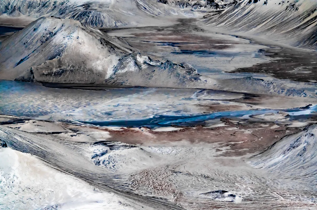 Aerial view of a blue river winding through snowy volcanic hills, Ofanfrá series — travel photography by Janina Laszlo