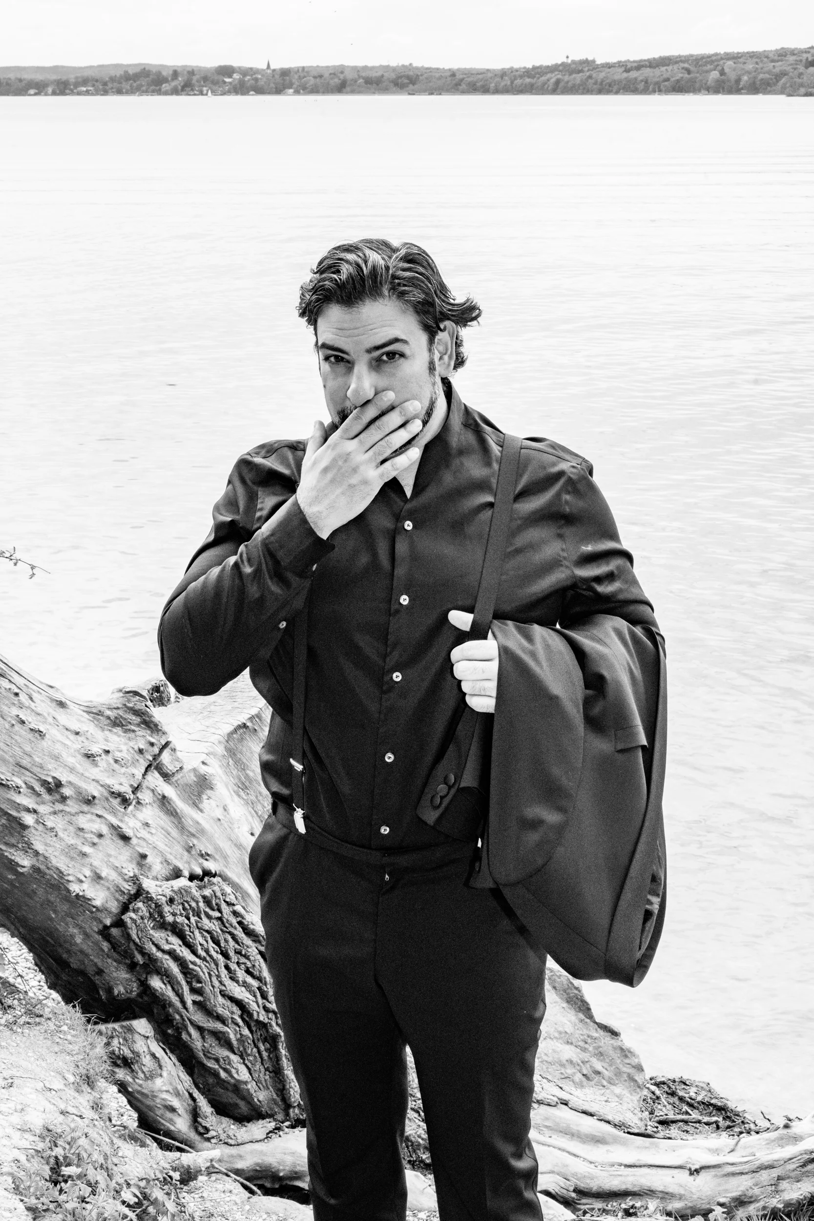 Black-and-white portrait of Ilker Arcayürek with his hand over his mouth, jacket over his shoulder — Ilker Arcayürek, artist portrait photography by Janina Laszlo