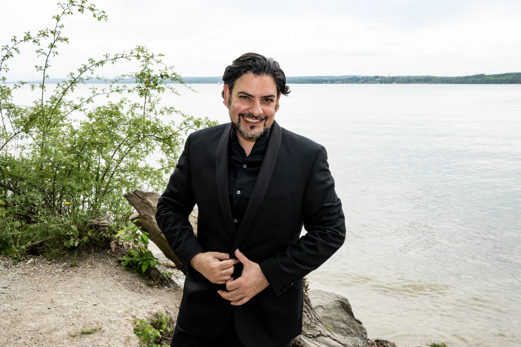 Ilker Arcayürek smiling in a black tuxedo on the lake shore — Ilker Arcayürek, artist portrait photography by Janina Laszlo