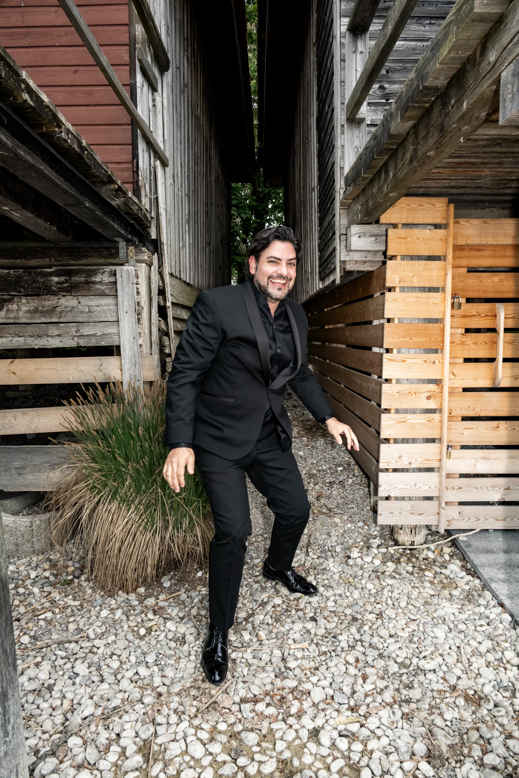 Ilker Arcayürek laughing in a tuxedo between old wooden boathouses — Ilker Arcayürek, artist portrait photography by Janina Laszlo