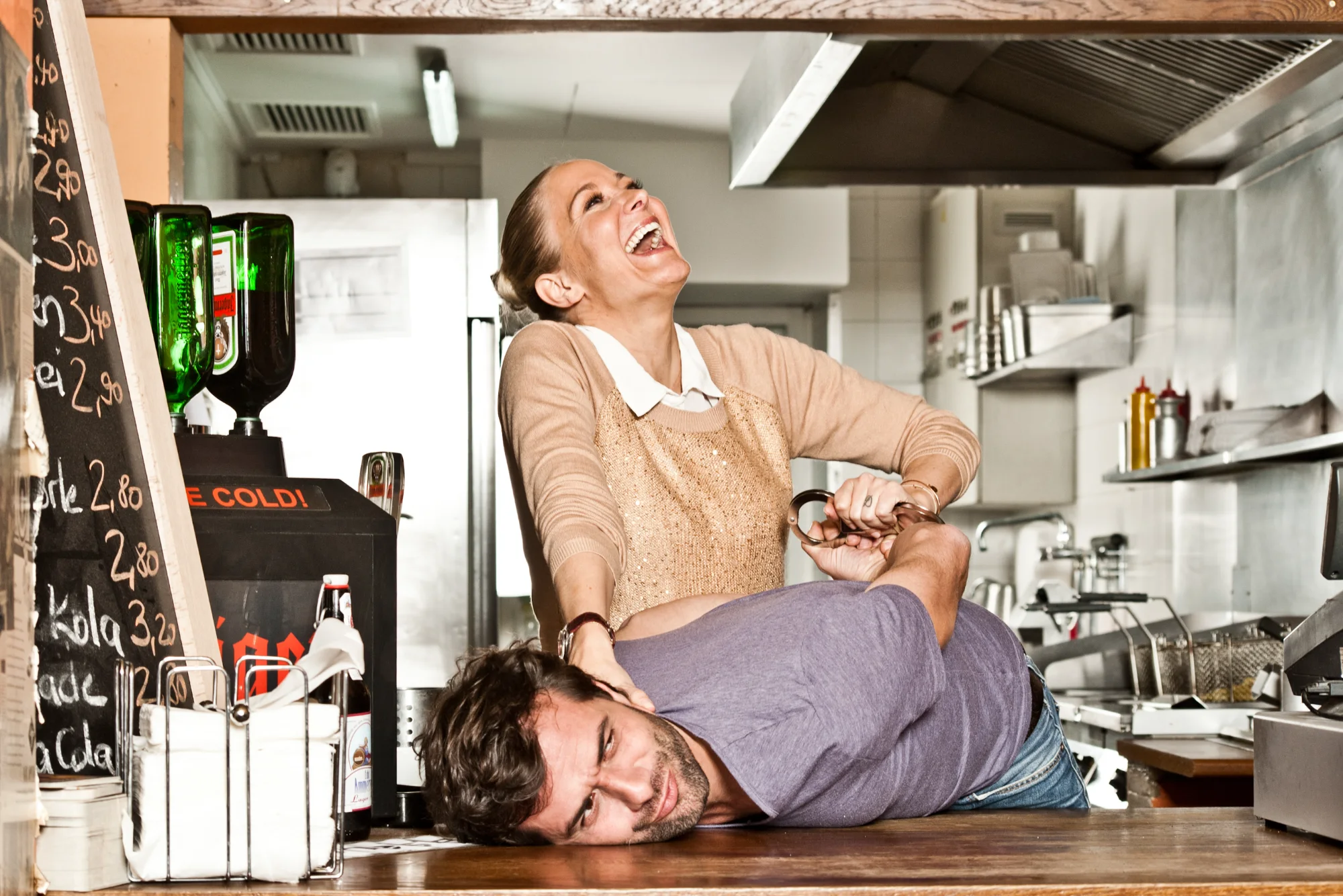 Kai Schumann lying across the counter, Janine Kunze leaning over him — IN Magazin, celebrity editorial photography by Janina Laszlo
