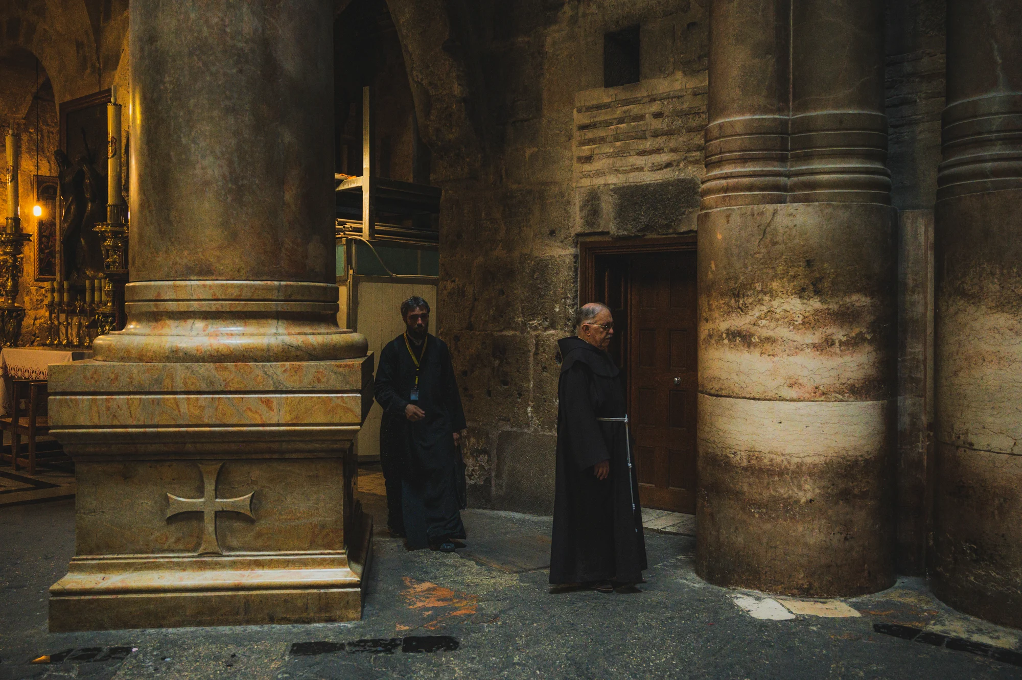 Franciscan friar and Orthodox monk among massive stone columns in the Church of the Holy Sepulchre, Old City of Jerusalem — Israel, travel and street photography by Janina Laszlo