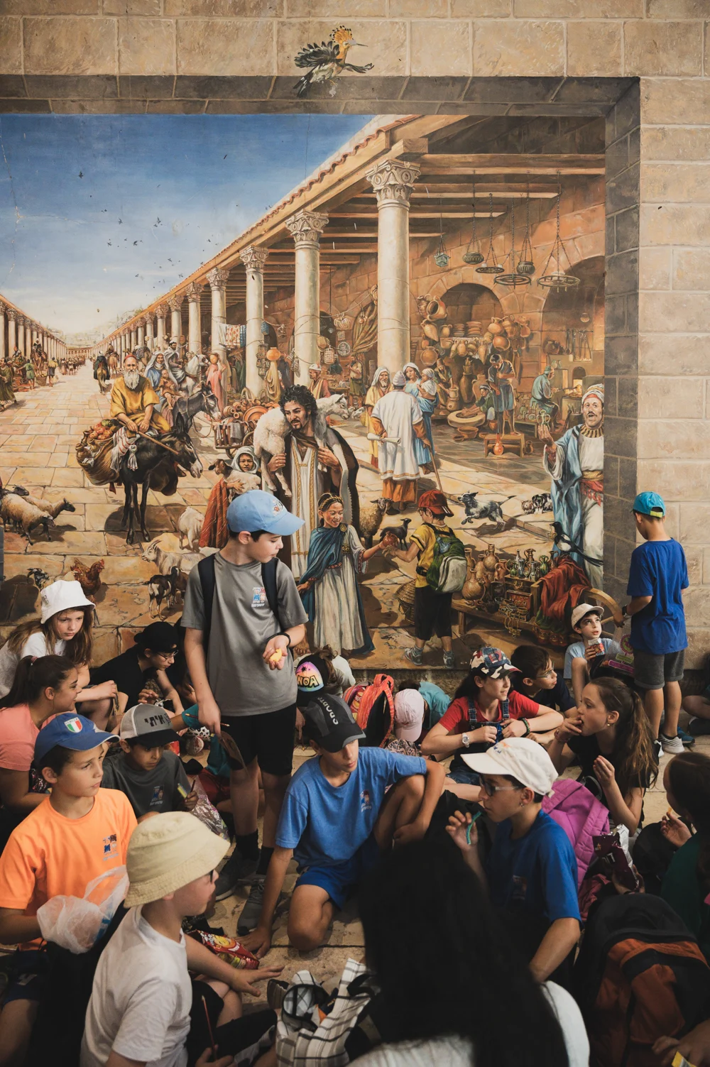 School children on an outing sitting before a painted mural of ancient Jerusalem's colonnaded market street, Jerusalem — Israel, travel and street photography by Janina Laszlo