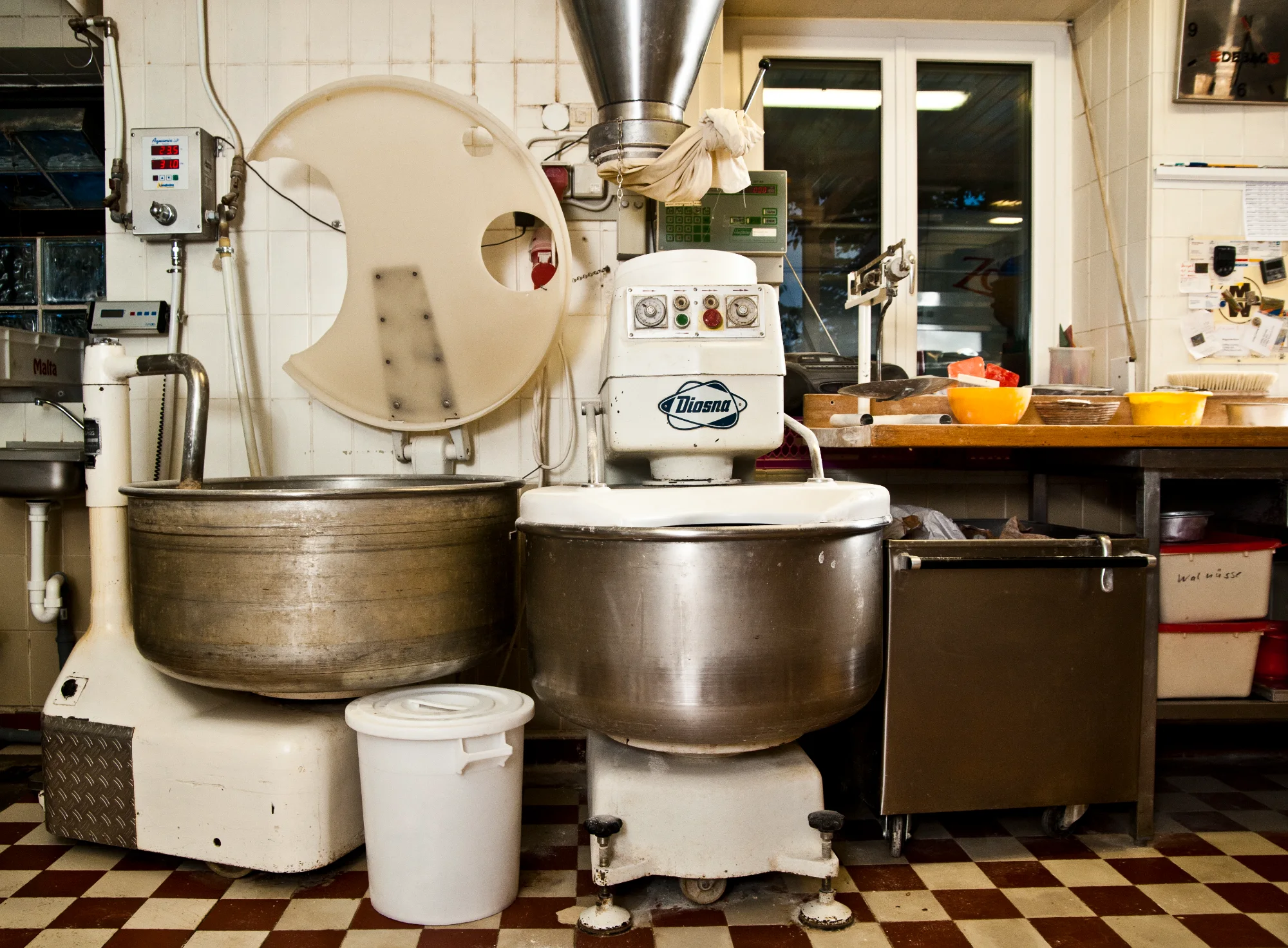 Two vintage spiral dough mixers with steel bowls on the red and white checkered tile floor — Landbäckerei Zobel, Seefeld, Bavaria, craft bakery photography by Janina Laszlo