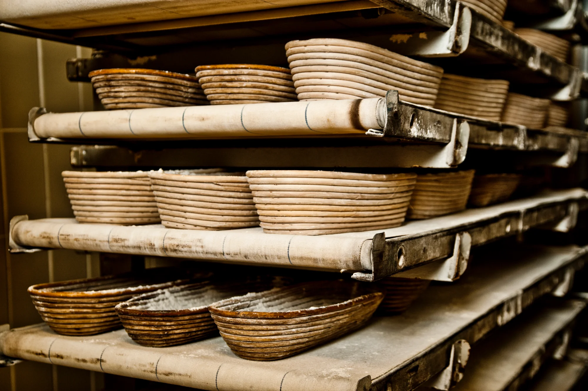 Rattan proofing baskets stacked on canvas-covered rack shelves — Landbäckerei Zobel, Seefeld, Bavaria, craft bakery photography by Janina Laszlo
