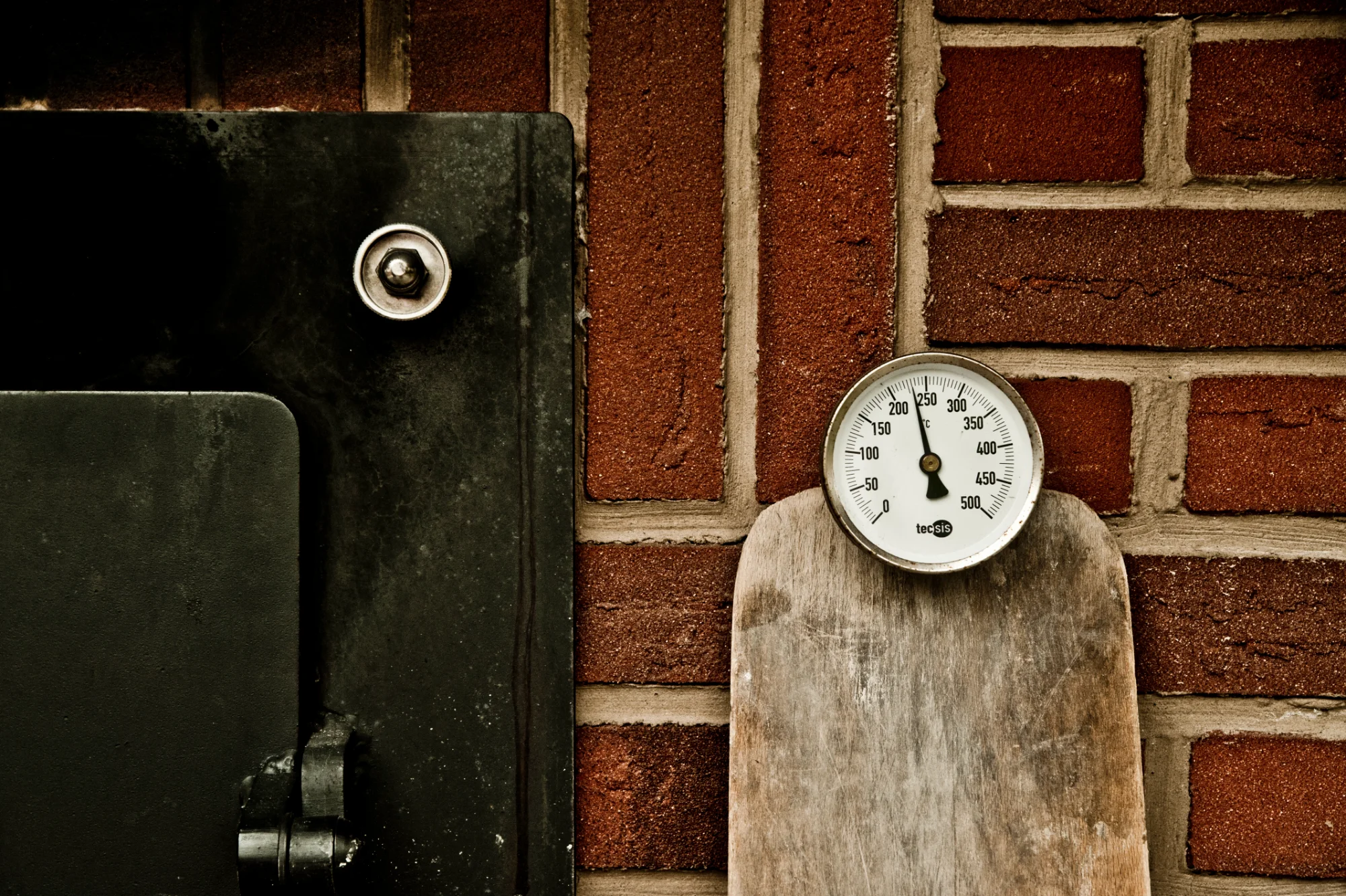 Oven thermometer and a worn wooden peel against a red brick wall beside the iron oven door — Landbäckerei Zobel, Seefeld, Bavaria, craft bakery photography by Janina Laszlo