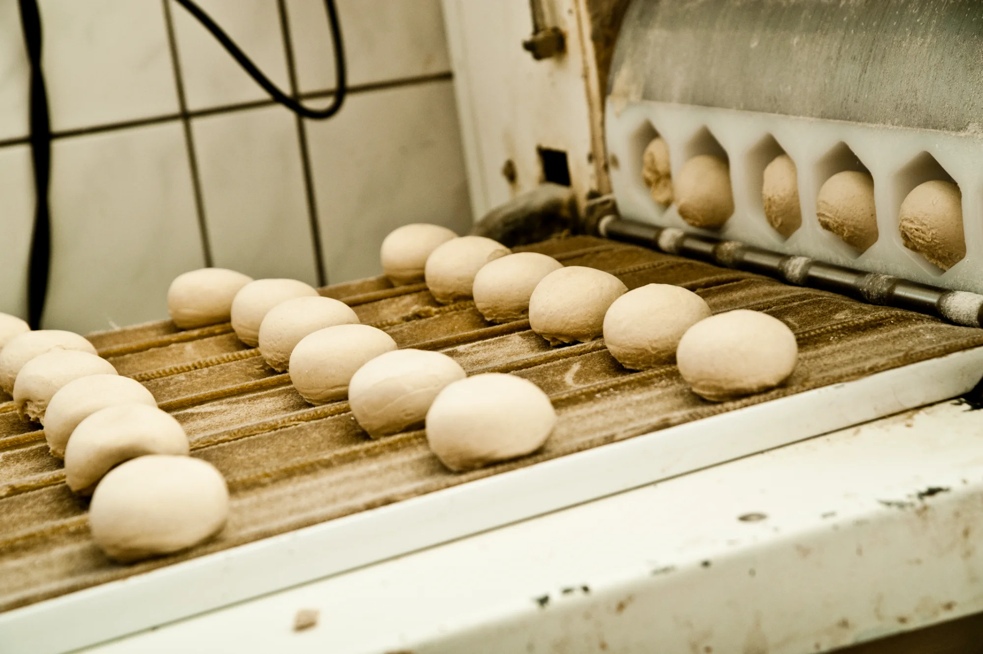 Rounded dough pieces leaving the roll divider on a floured conveyor belt — Landbäckerei Zobel, Seefeld, Bavaria, craft bakery photography by Janina Laszlo