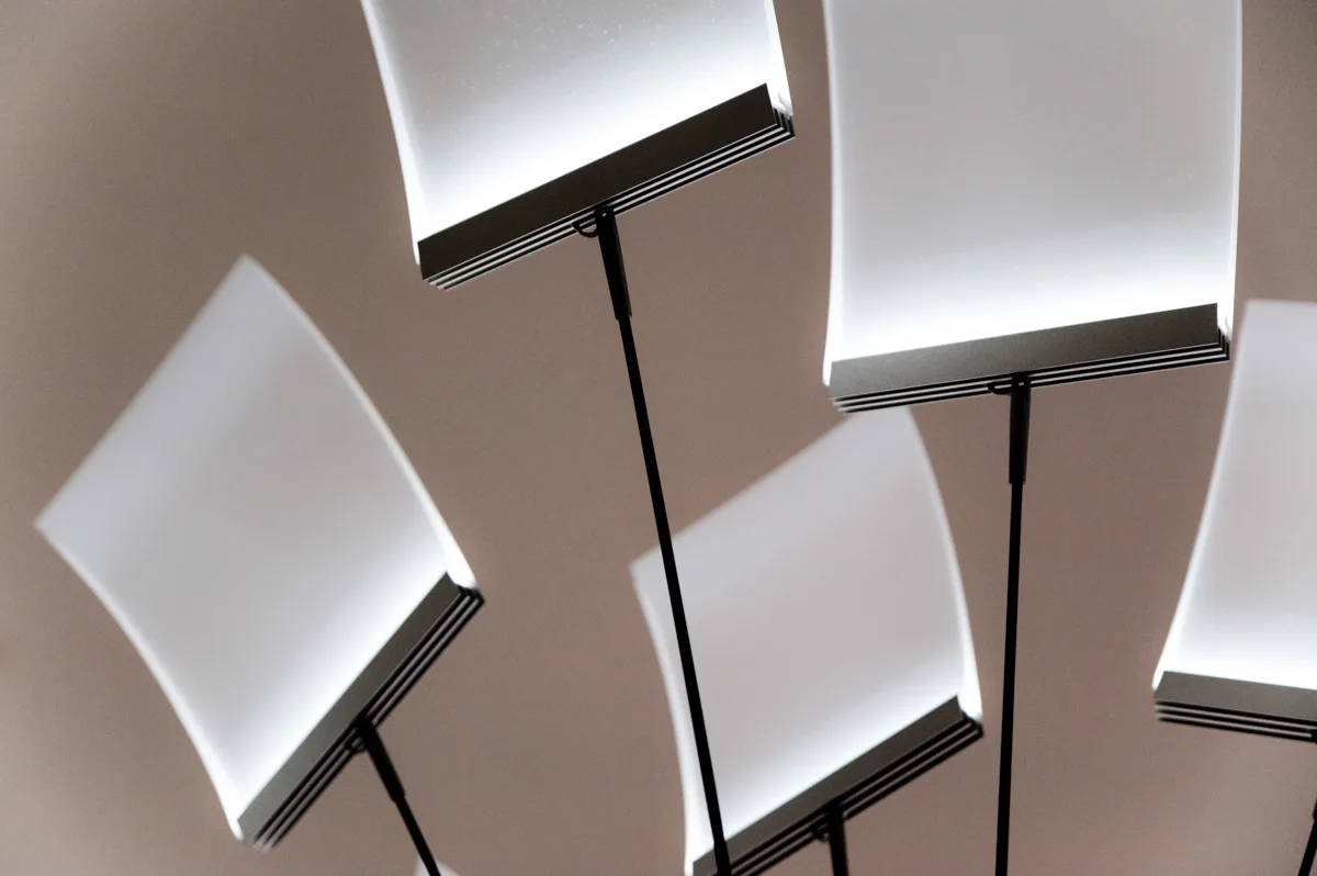 Illuminated white panels of the LC 1.0 chandelier on slender black rods, warm background — LC 1.0 chandelier by Denise M. Hachinger, product and design photography by Janina Laszlo