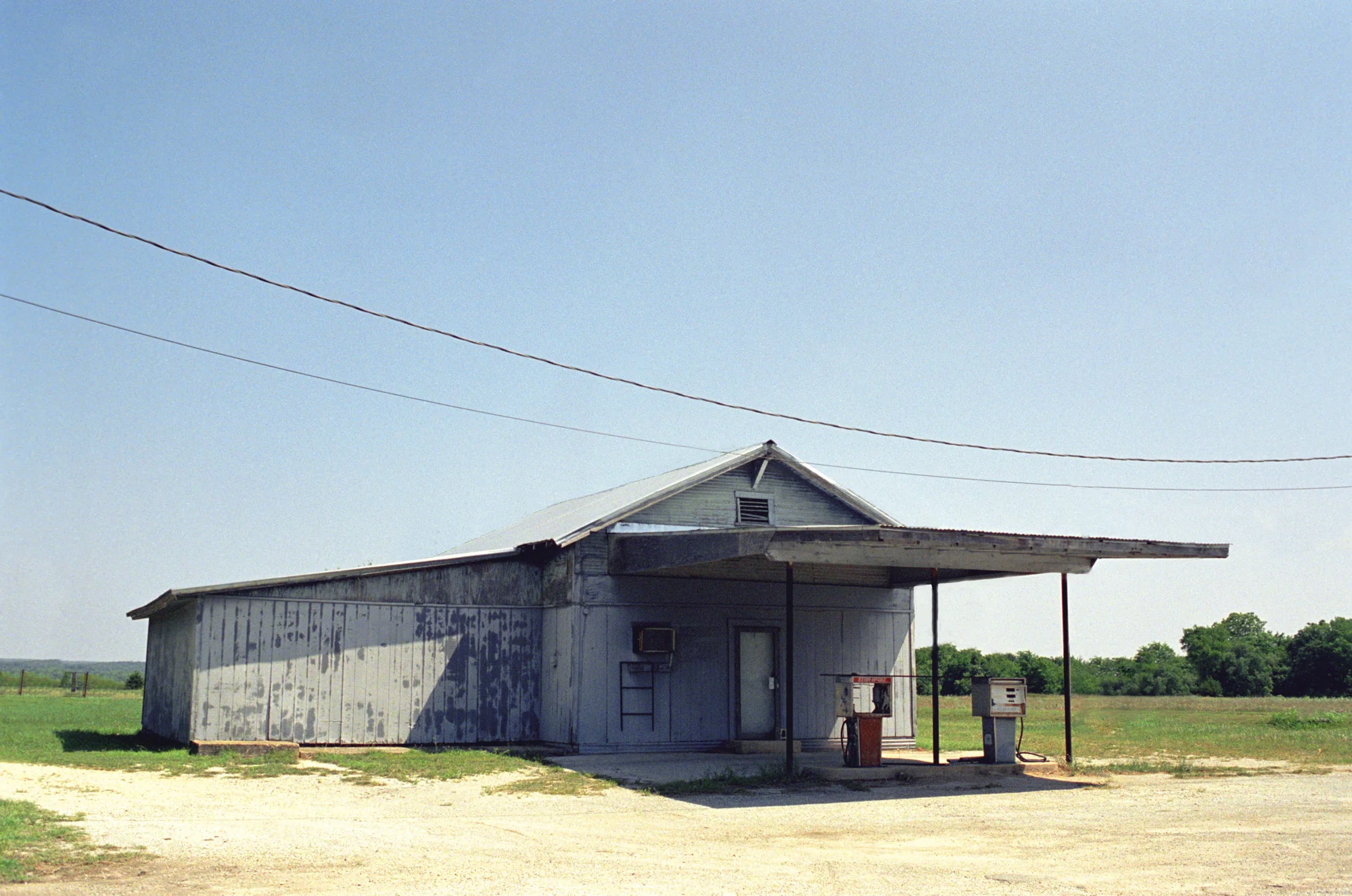 Weathered wooden country store with a corrugated roof and old fuel pumps under the canopy — Love County, Oklahoma, analog documentary photography by Janina Laszlo