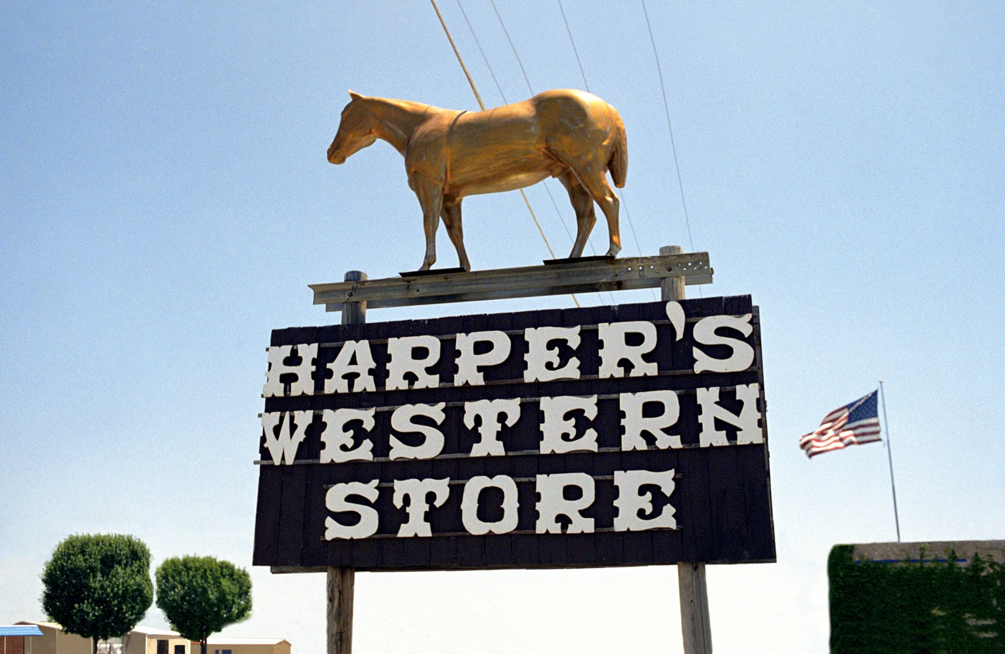 Golden horse statue on the Harper's Western Store sign with an American flag — Love County, Oklahoma, analog documentary photography by Janina Laszlo