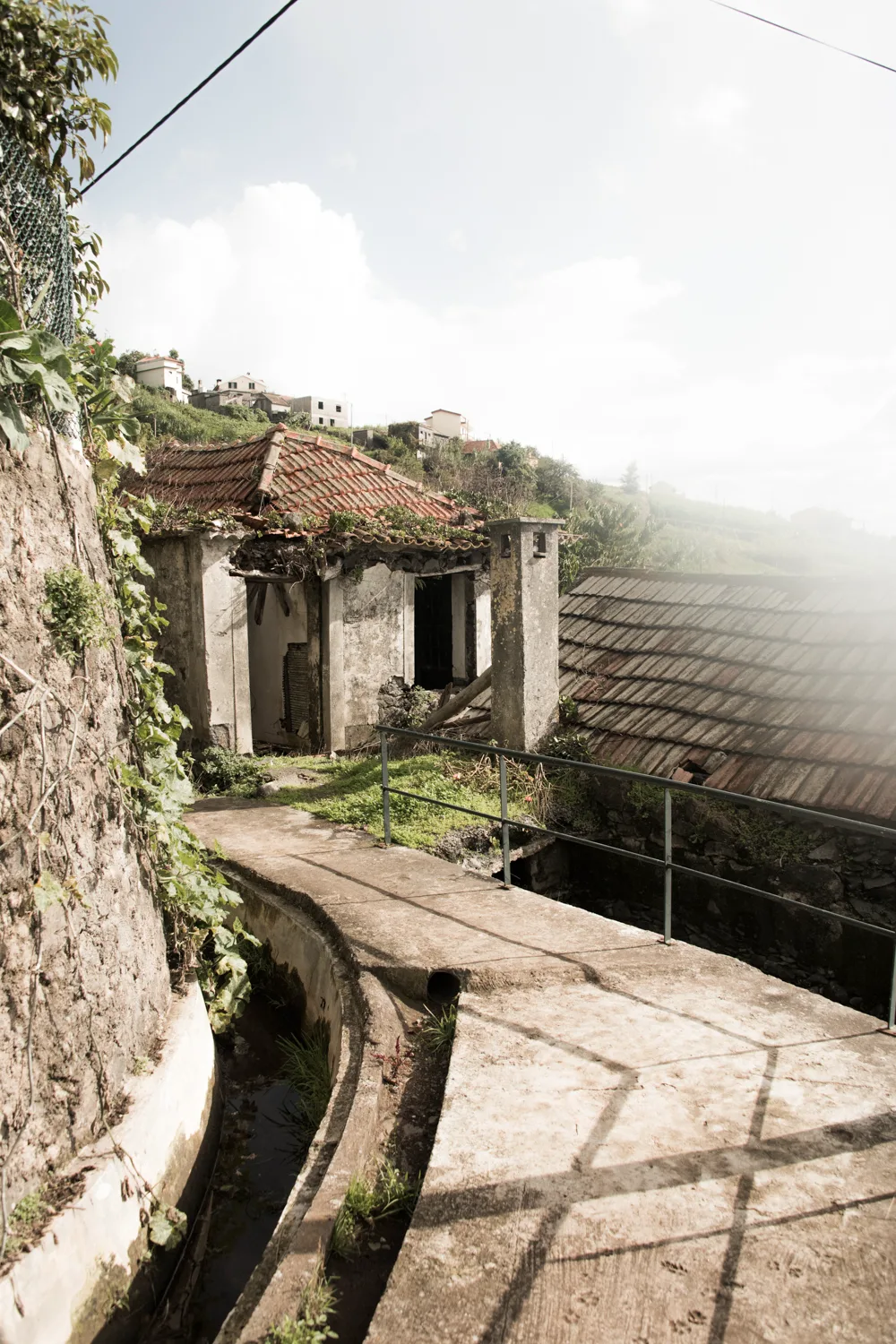 Levada channel along a path past a derelict tiled-roof house on a terraced hillside — Madeira, landscape and travel photography by Janina Laszlo