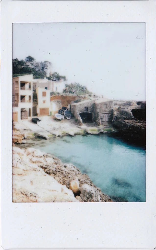Polaroid of a turquoise rocky cove with stone houses and boathouses on the cliffs, Mallorca — Mallorca Polaroids, analog travel photography by Janina Laszlo