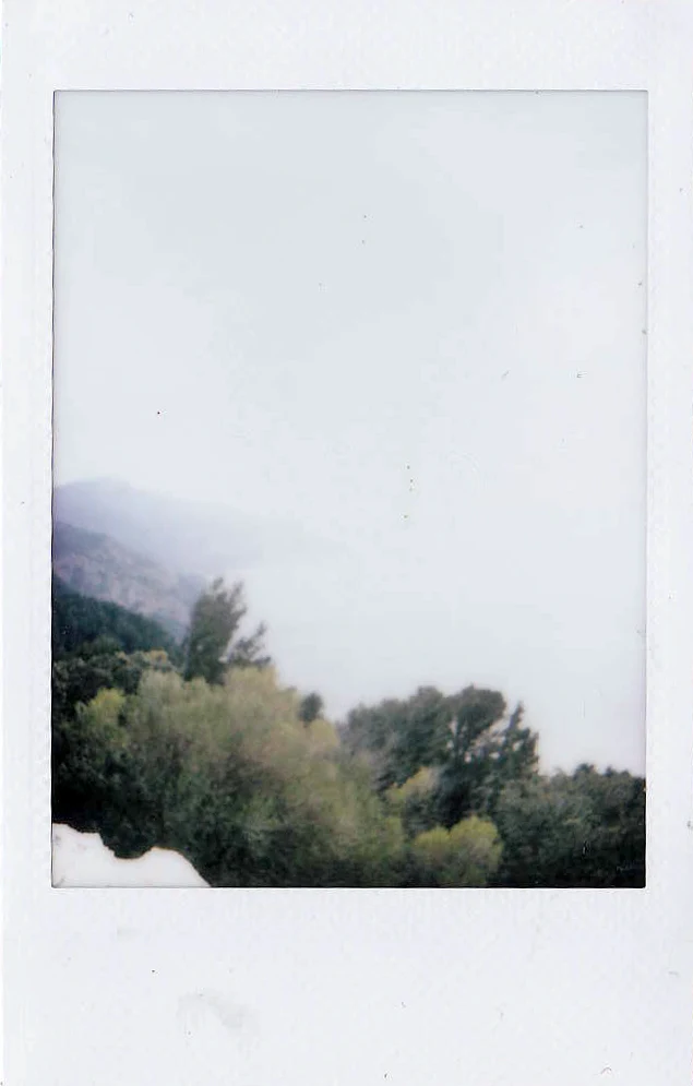 Polaroid of a hazy mountain view over pine forest, faded instant-film tones, Mallorca — Mallorca Polaroids, analog travel photography by Janina Laszlo