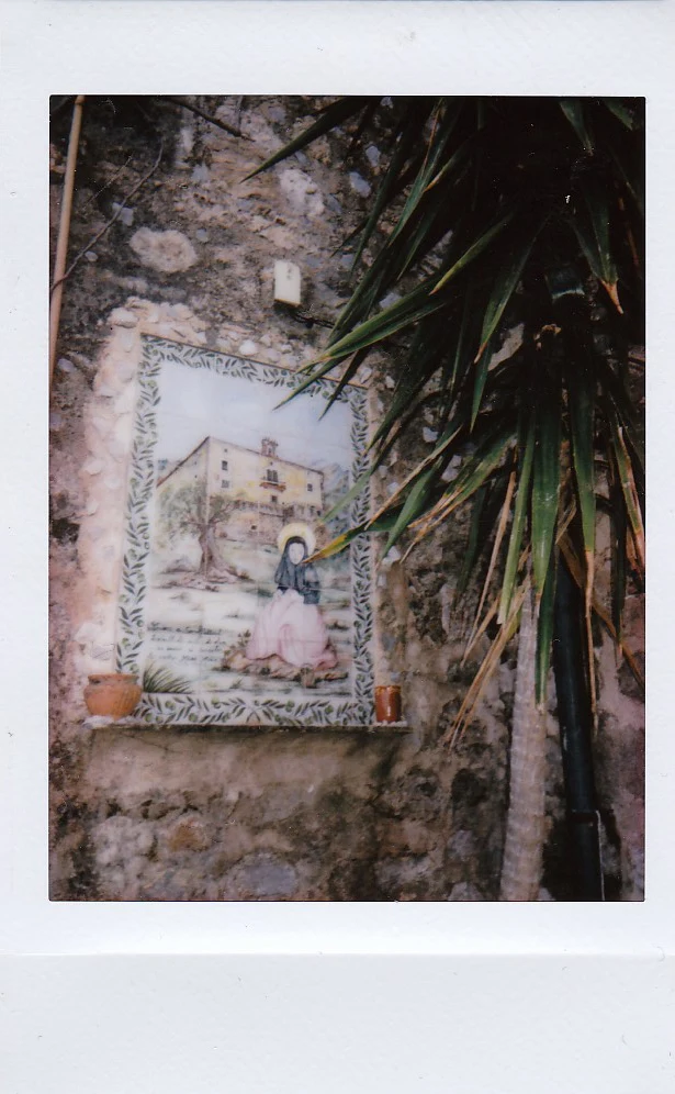 Polaroid of a hand-painted ceramic tile shrine set into a stone wall beside a palm, Mallorca — Mallorca Polaroids, analog travel photography by Janina Laszlo