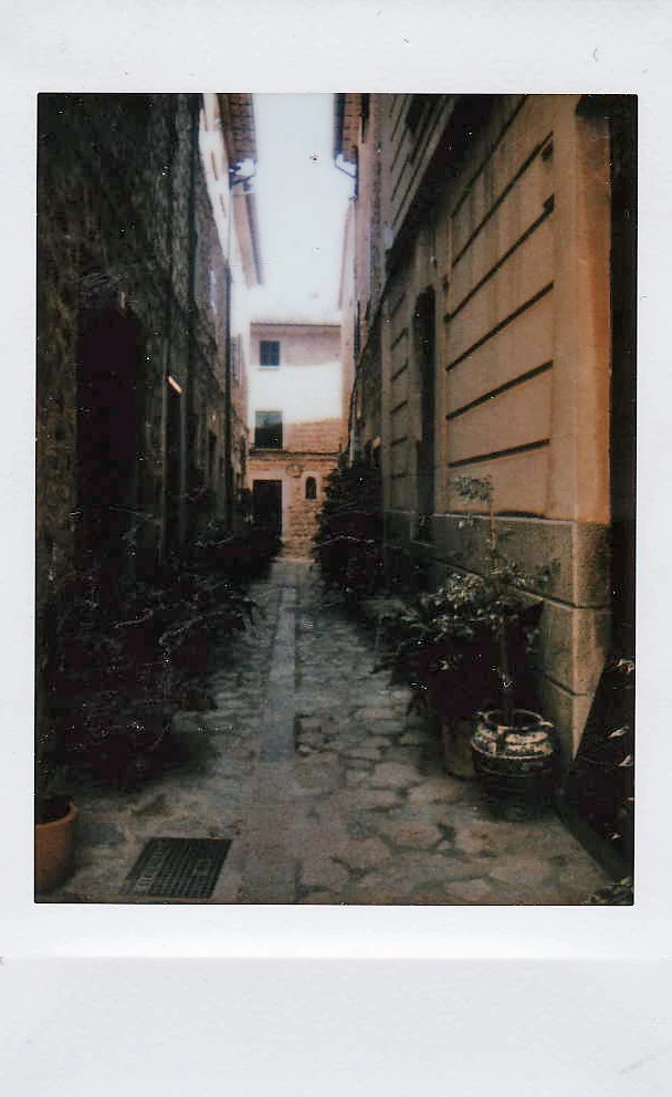 Polaroid of a narrow cobbled lane between ochre stone houses with potted plants, Mallorca — Mallorca Polaroids, analog travel photography by Janina Laszlo