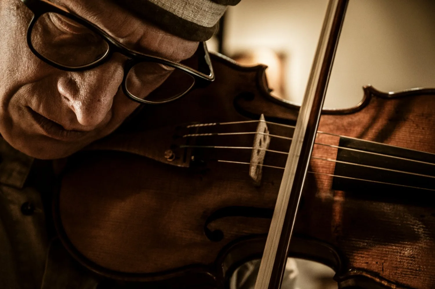 Martin Schleske playing one of his violins, close-up with glasses in warm workshop light — Martin Schleske, master violin maker, editorial portrait and documentary photography by Janina Laszlo, Landsberg am Lech