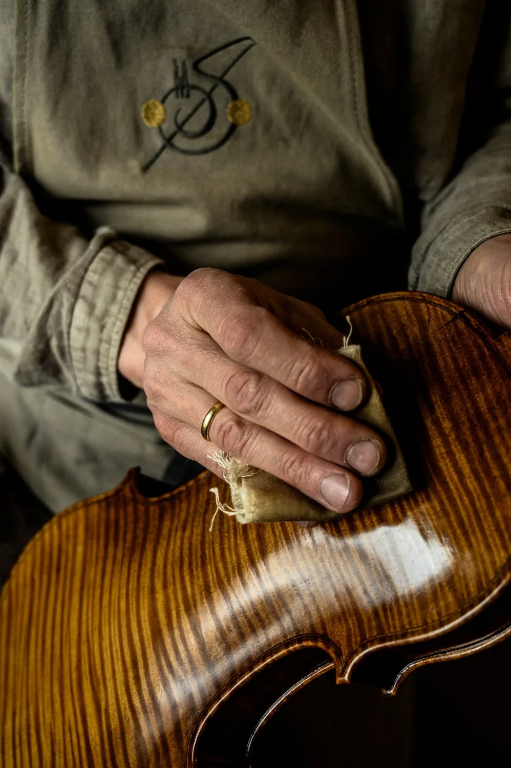 Hands polishing the flamed maple back of a varnished violin — Martin Schleske, master violin maker, editorial portrait and documentary photography by Janina Laszlo, Landsberg am Lech