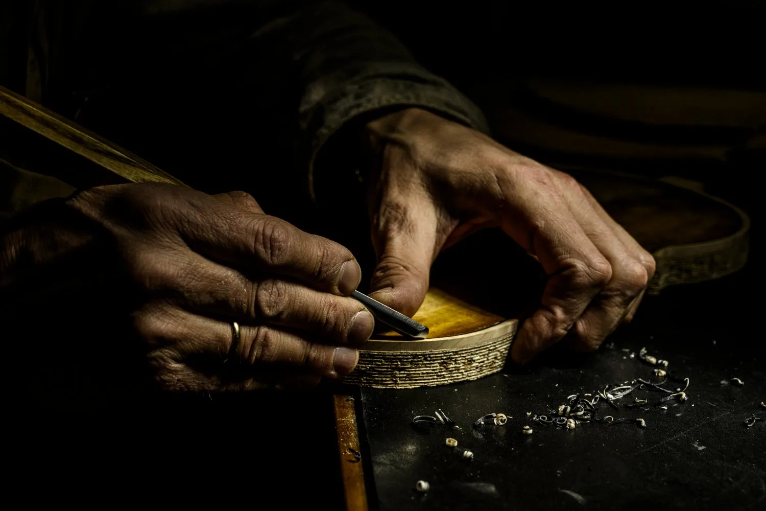 Hands carving a violin rib with a knife among wood shavings — Martin Schleske, master violin maker, editorial portrait and documentary photography by Janina Laszlo, Landsberg am Lech