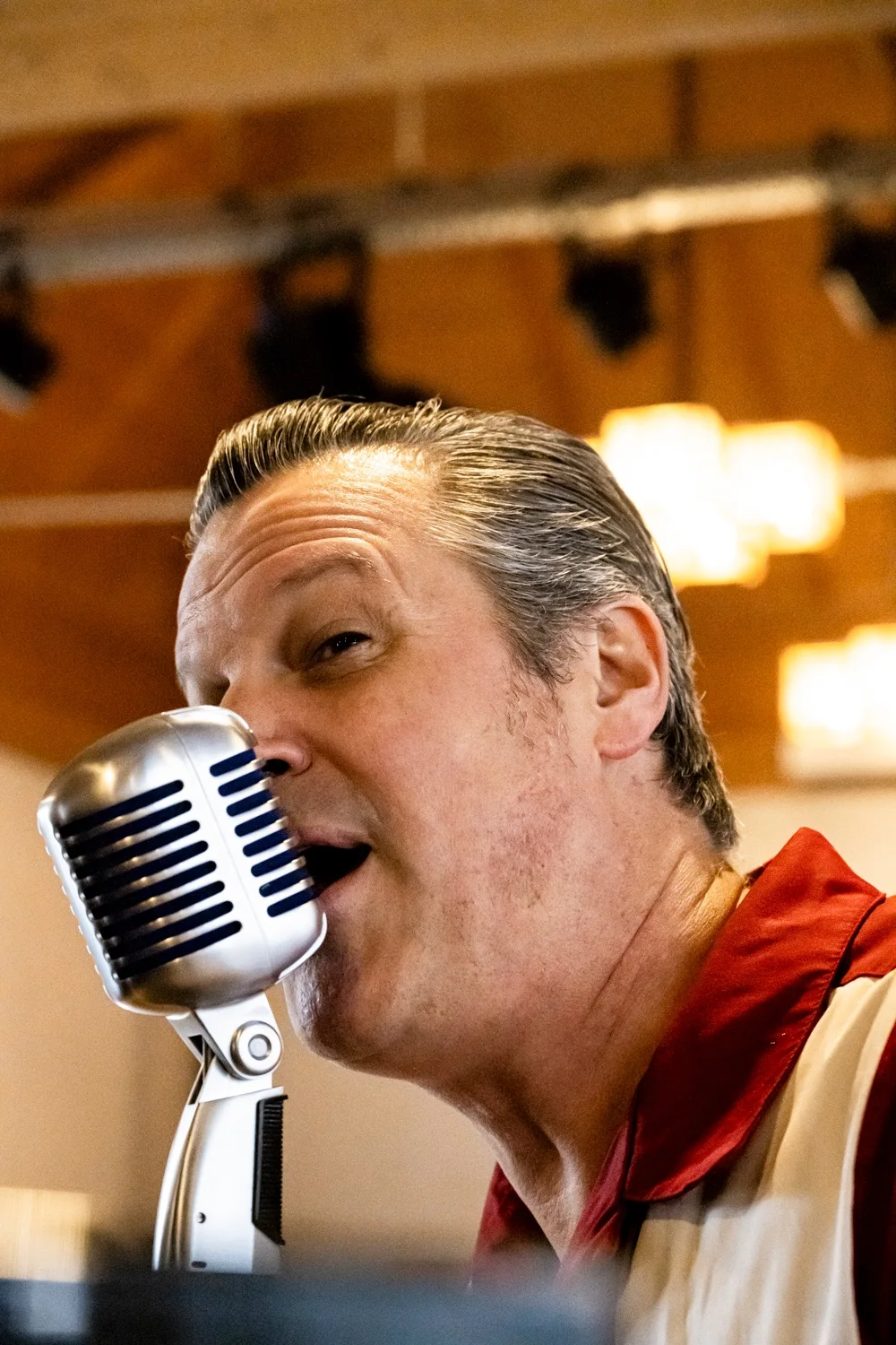 Matthias Heiligensetzer singing into a vintage microphone in a red and white bowling shirt — Matthias Heiligensetzer, pianist & entertainer, musician portrait photography by Janina Laszlo, Munich