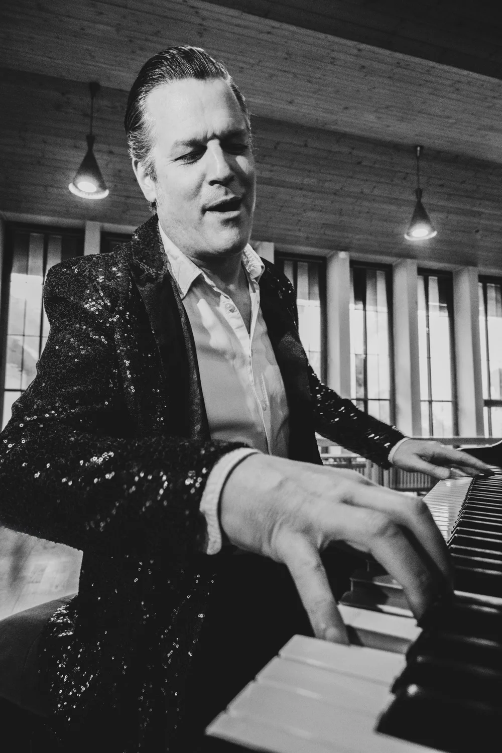 Matthias Heiligensetzer singing with closed eyes at the piano in a sequin jacket, black-and-white — Matthias Heiligensetzer, pianist & entertainer, musician portrait photography by Janina Laszlo, Munich
