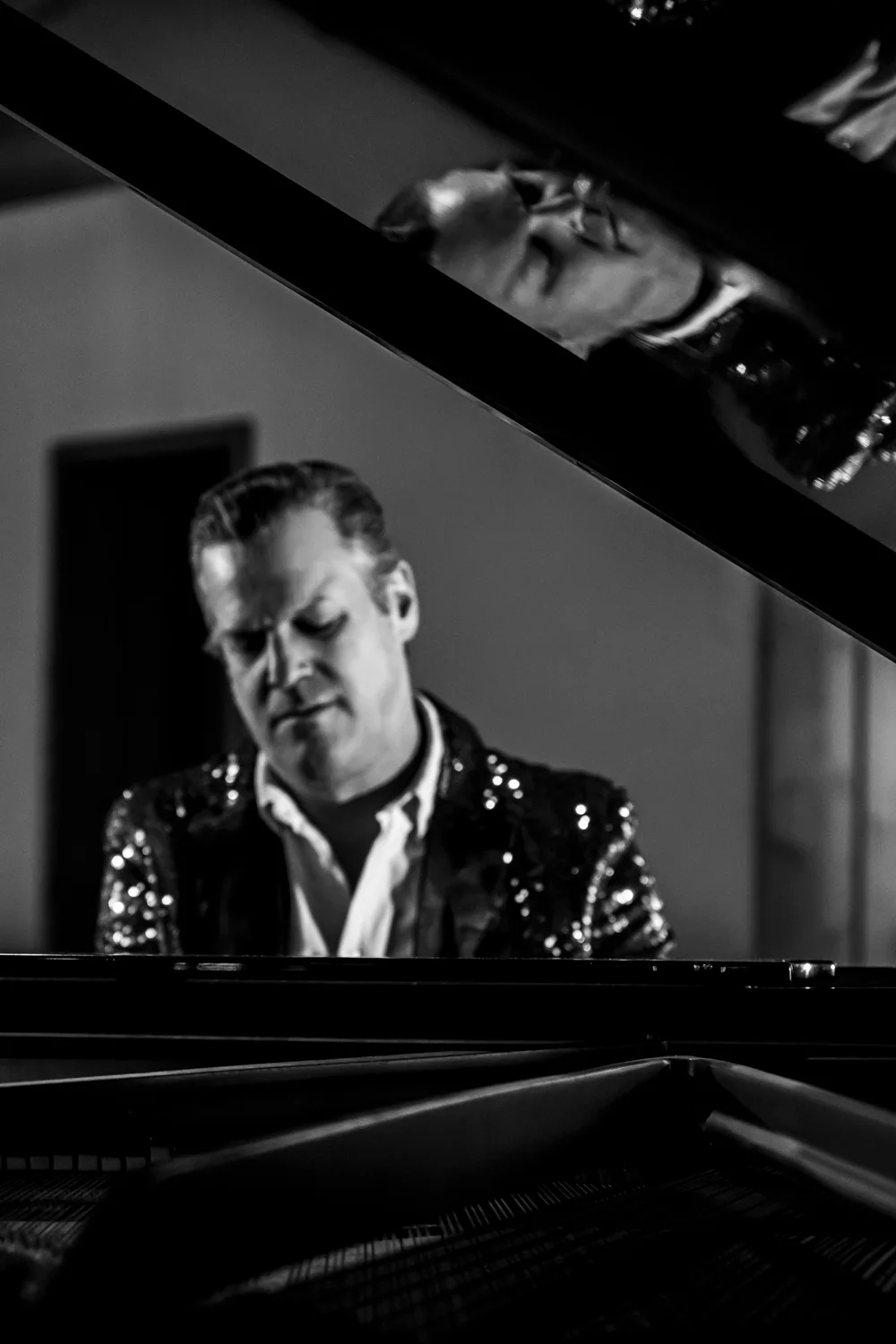 Matthias Heiligensetzer in a sequin jacket seen through the open lid of a grand piano, black-and-white — Matthias Heiligensetzer, pianist & entertainer, musician portrait photography by Janina Laszlo, Munich