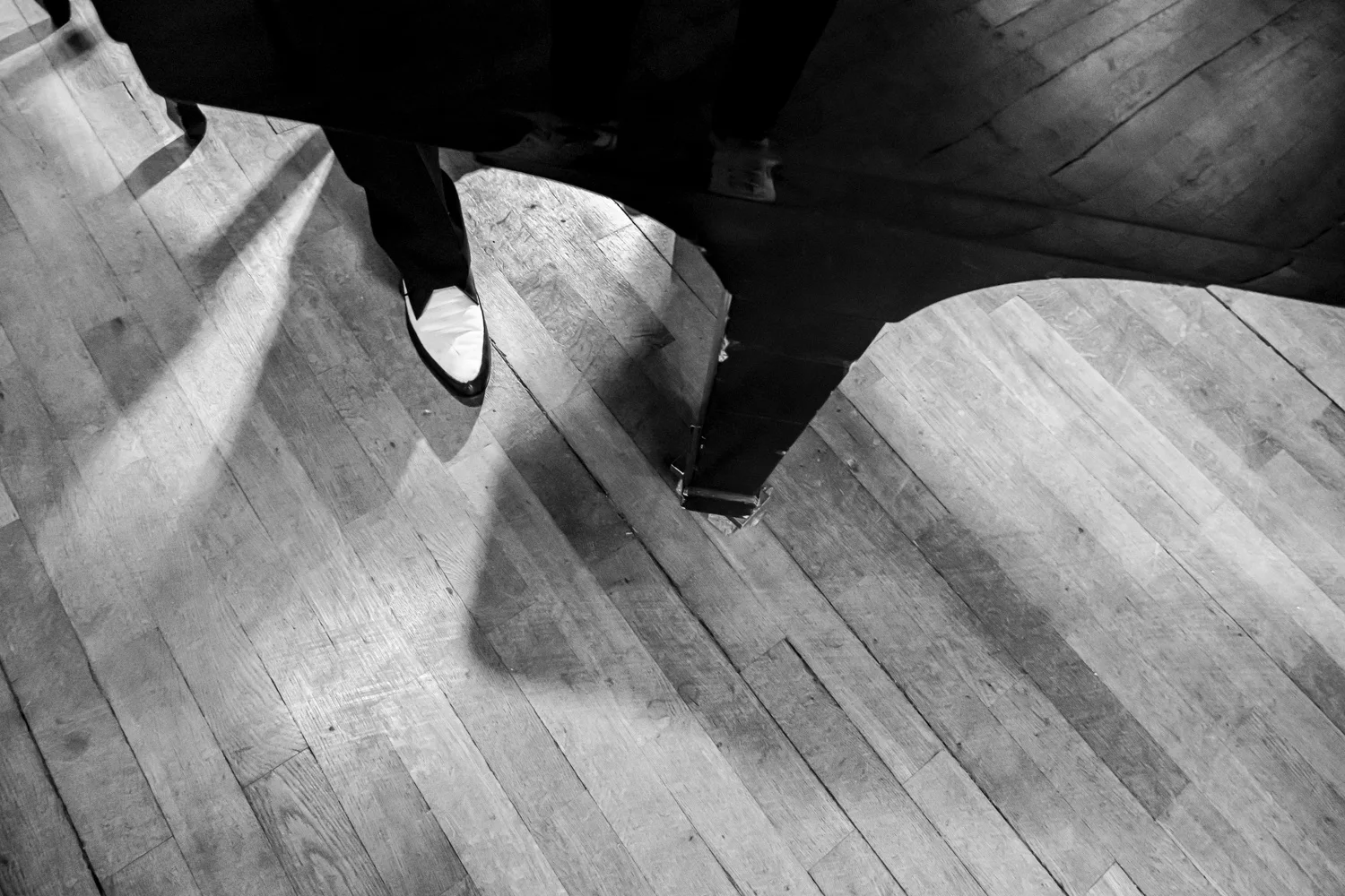 Two-tone shoe and piano leg on a sunlit wooden floor seen from above, black-and-white — Matthias Heiligensetzer, pianist & entertainer, musician portrait photography by Janina Laszlo, Munich
