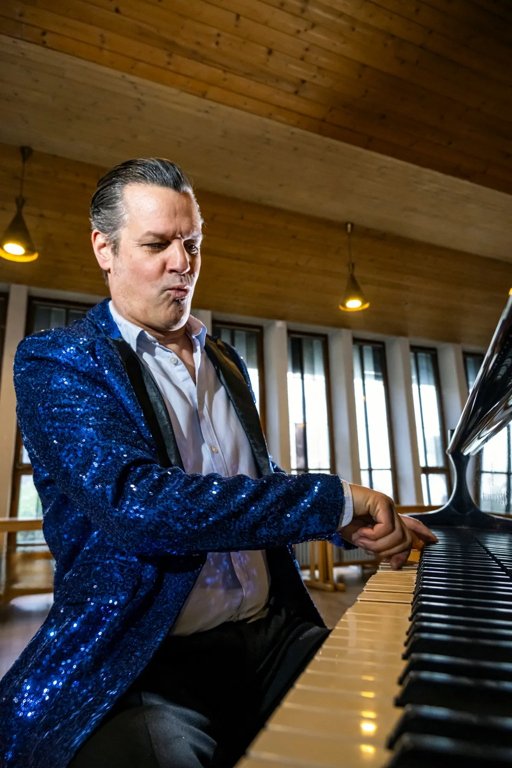 Matthias Heiligensetzer playing piano in a blue sequin jacket in a wood-panelled hall — Matthias Heiligensetzer, pianist & entertainer, musician portrait photography by Janina Laszlo, Munich