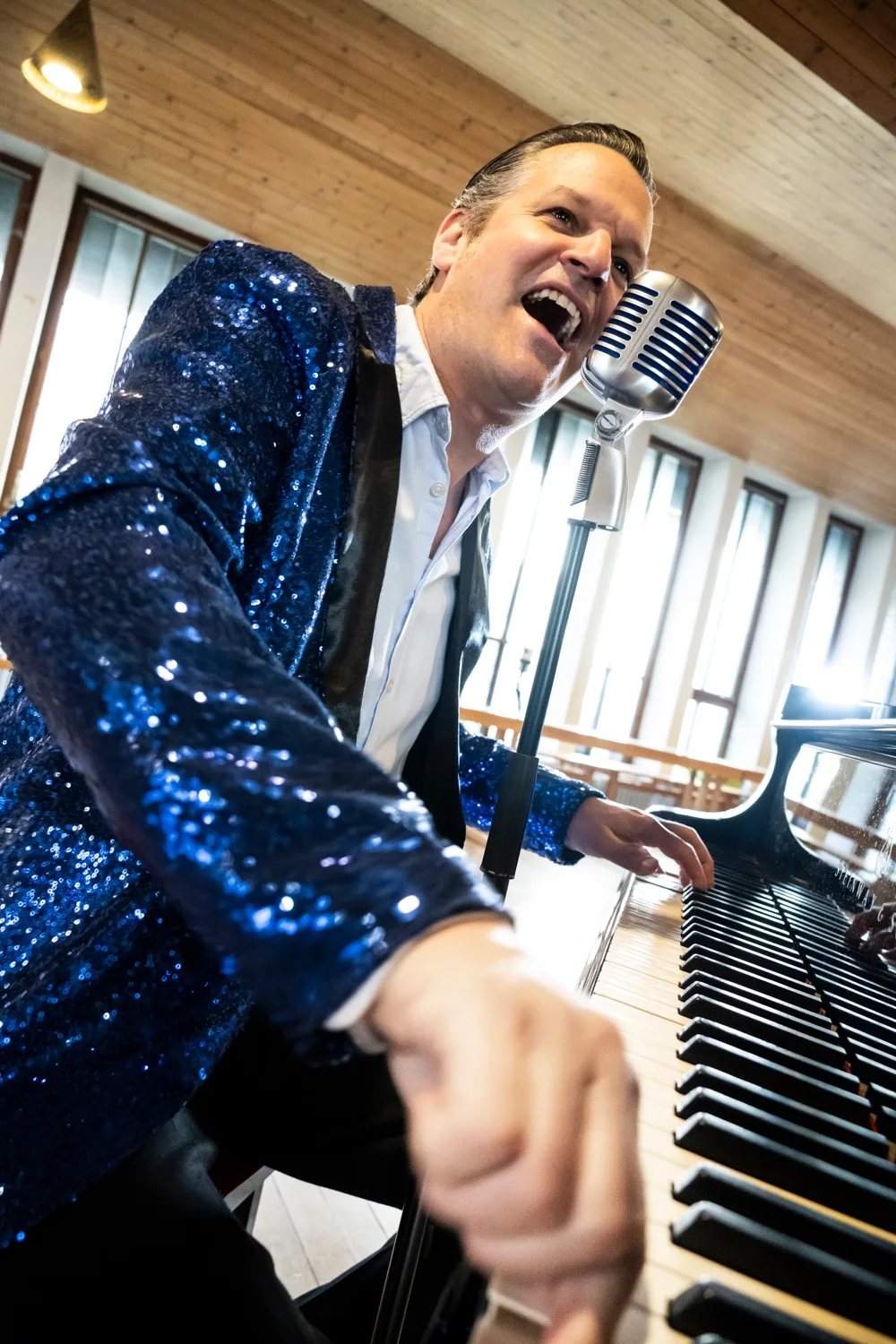 Matthias Heiligensetzer singing into a vintage microphone at the piano in a blue sequin jacket — Matthias Heiligensetzer, pianist & entertainer, musician portrait photography by Janina Laszlo, Munich