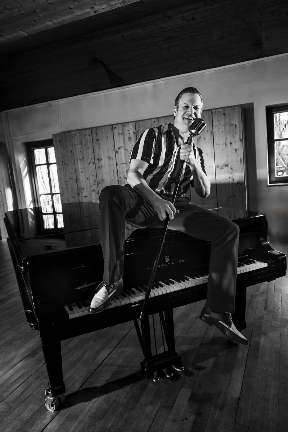 Matthias Heiligensetzer sitting on a Steinway grand piano with a vintage microphone, black-and-white — Matthias Heiligensetzer, pianist & entertainer, musician portrait photography by Janina Laszlo, Munich
