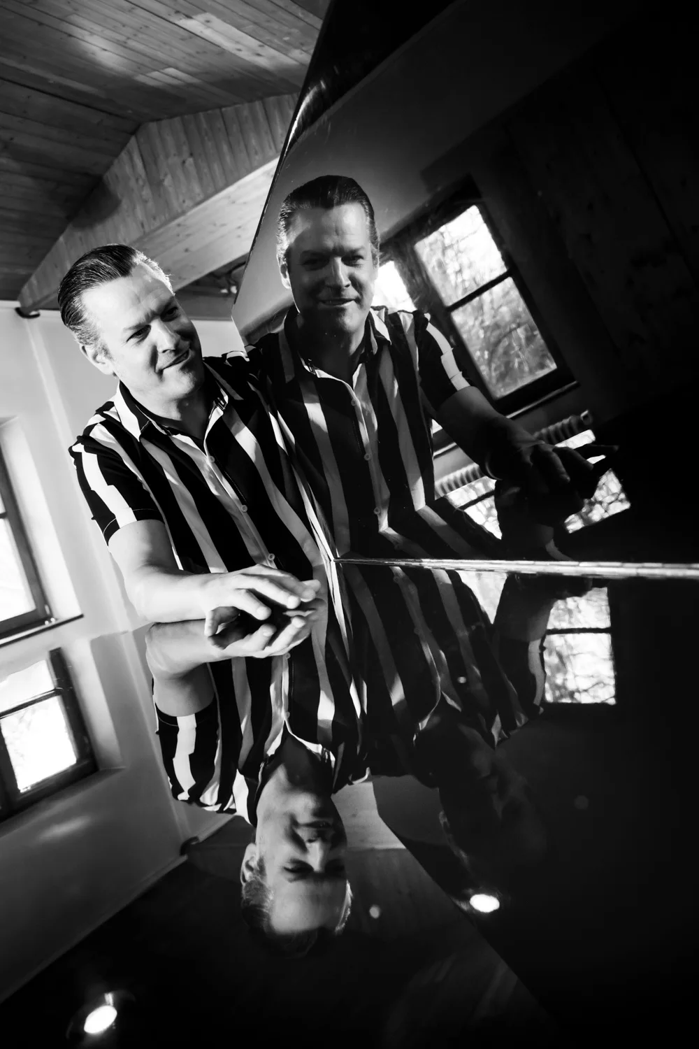 Matthias Heiligensetzer in a striped shirt reflected in the lacquered lid of a grand piano, black-and-white — Matthias Heiligensetzer, pianist & entertainer, musician portrait photography by Janina Laszlo, Munich