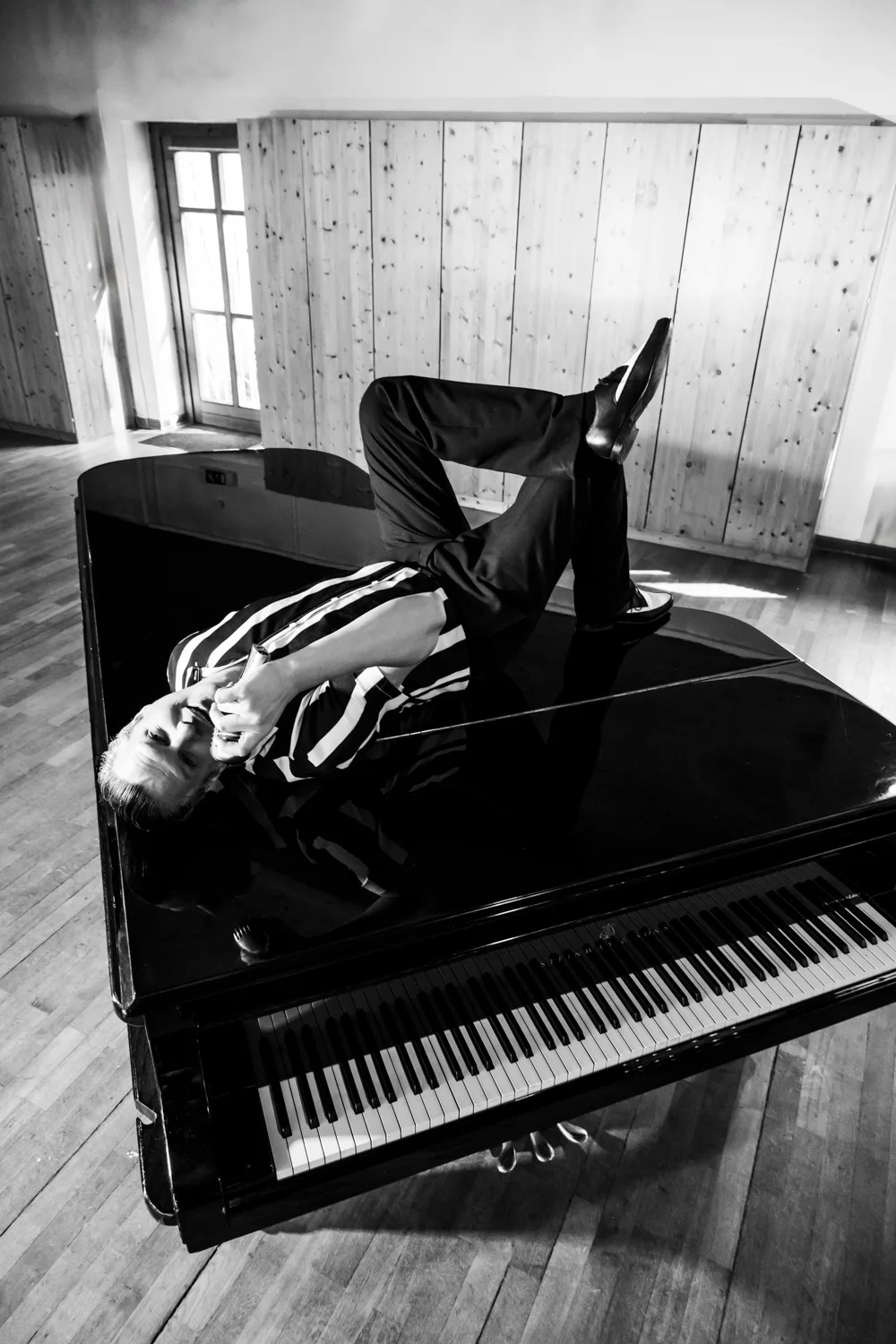 Matthias Heiligensetzer lying on top of a grand piano with his legs in the air, black-and-white — Matthias Heiligensetzer, pianist & entertainer, musician portrait photography by Janina Laszlo, Munich