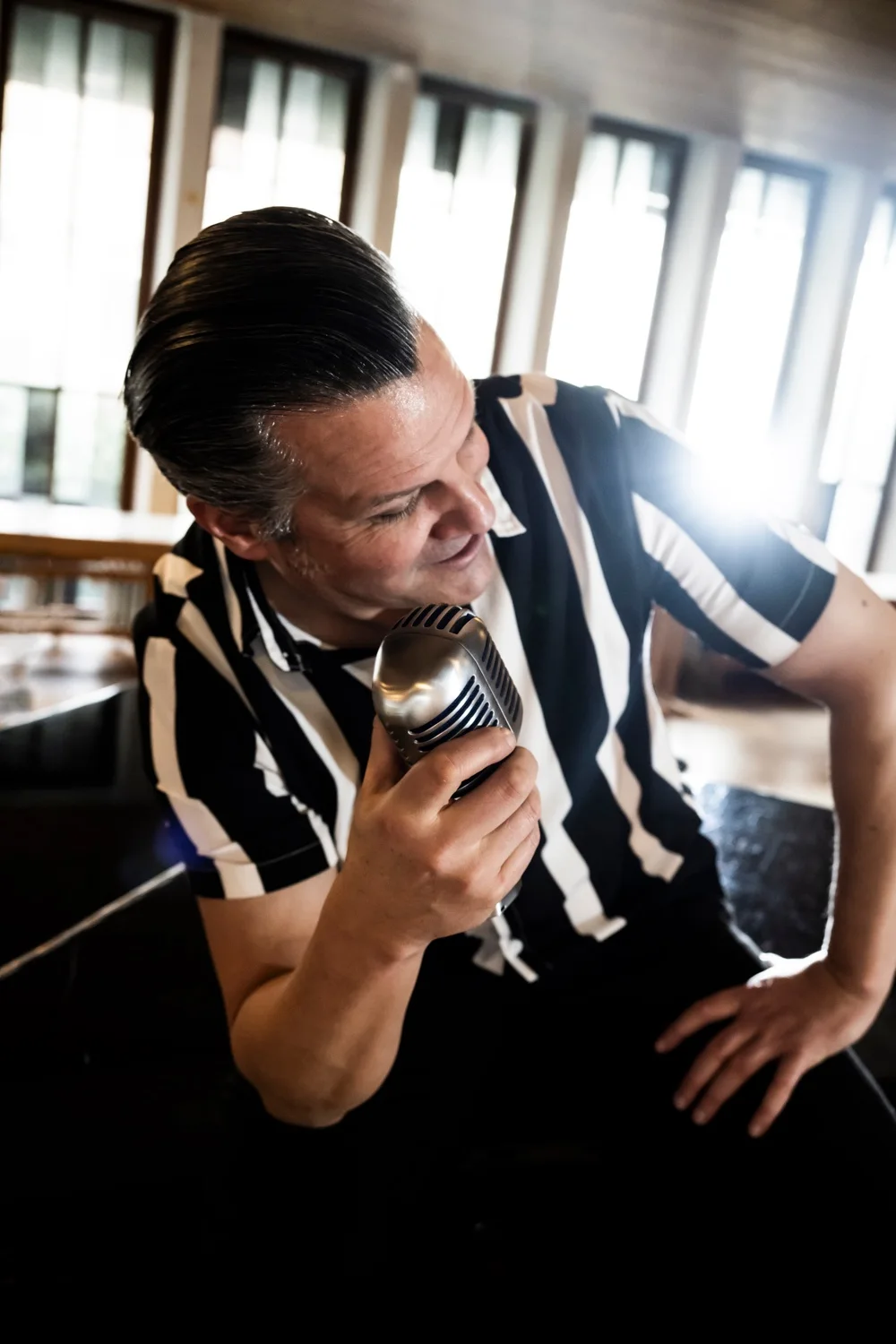 Matthias Heiligensetzer in a striped shirt holding a vintage microphone in backlight — Matthias Heiligensetzer, pianist & entertainer, musician portrait photography by Janina Laszlo, Munich