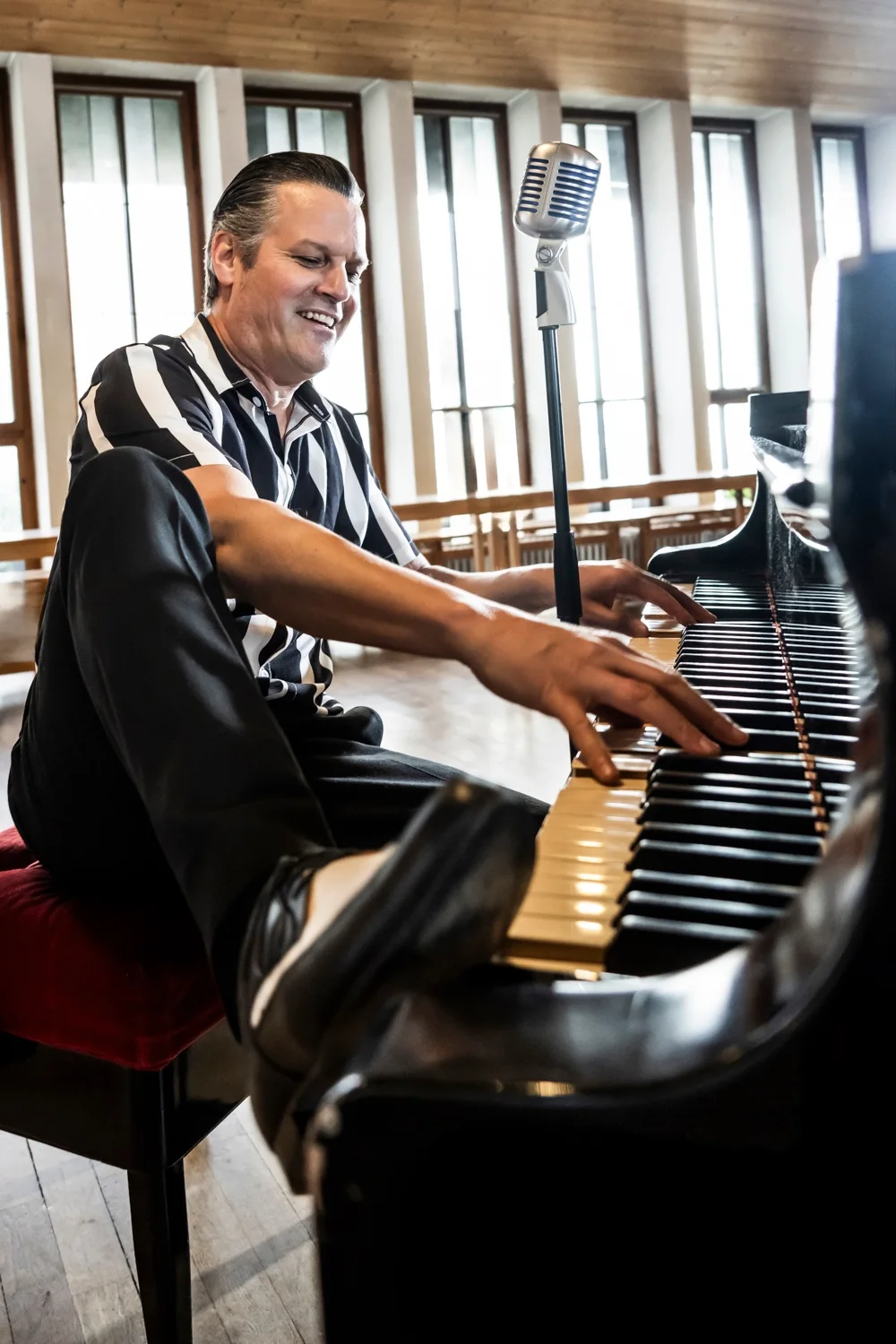 Matthias Heiligensetzer smiling at the piano with one foot raised on the keys — Matthias Heiligensetzer, pianist & entertainer, musician portrait photography by Janina Laszlo, Munich