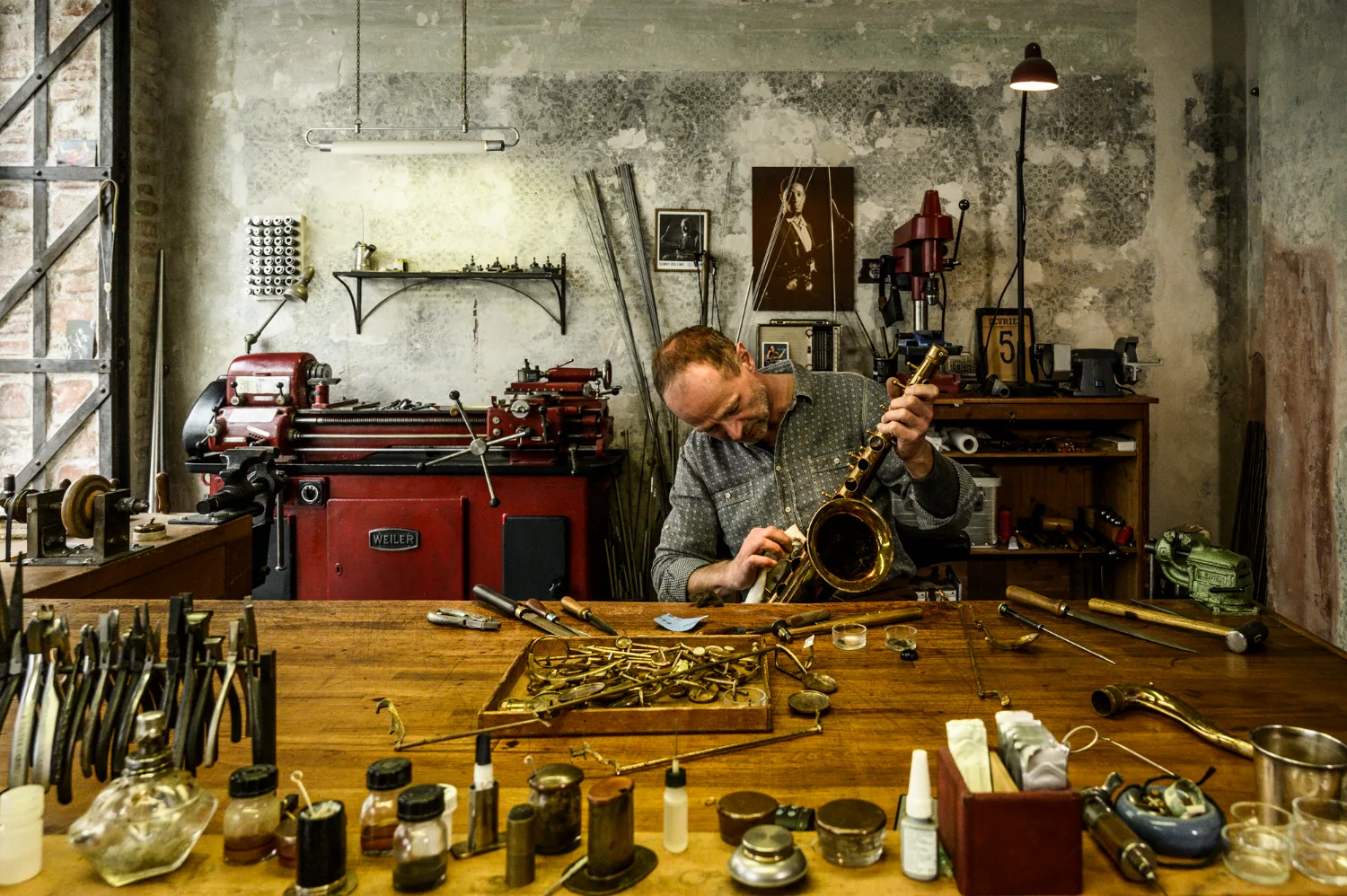 Max Frei at the workbench of his saxophone workshop, full view with lathe, tools and jazz portraits — Max Frei, saxophone workshop in Icking near Munich, corporate portraits and editorial photography by Janina Laszlo