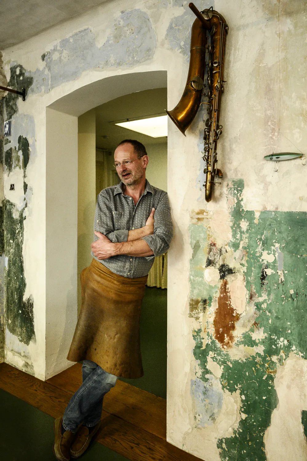 Max Frei leaning in the arched doorway of his workshop with a baritone saxophone on the wall — Max Frei, saxophone workshop in Icking near Munich, corporate portraits and editorial photography by Janina Laszlo