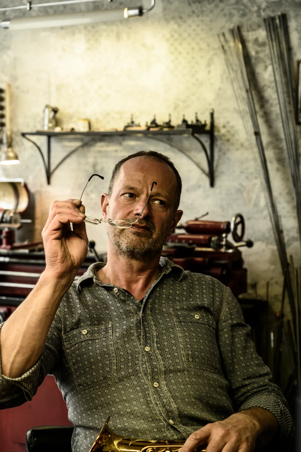Portrait of Max Frei with his glasses in hand, workshop behind him — Max Frei, saxophone workshop in Icking near Munich, corporate portraits and editorial photography by Janina Laszlo