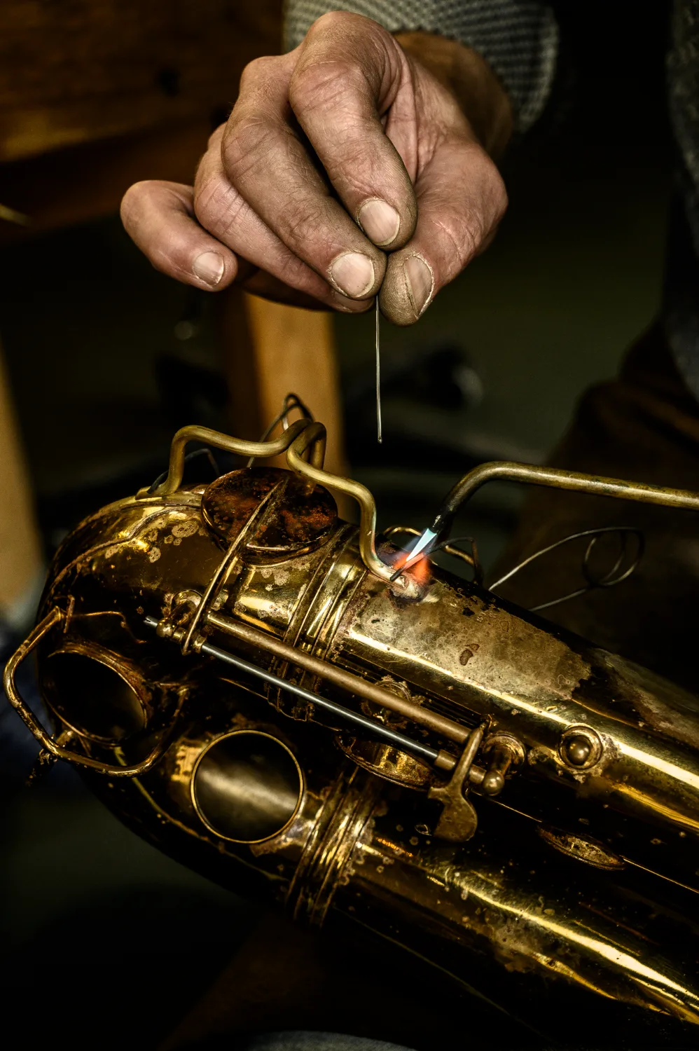 Hands soldering a saxophone key guard with a small flame — Max Frei, saxophone workshop in Icking near Munich, corporate portraits and editorial photography by Janina Laszlo