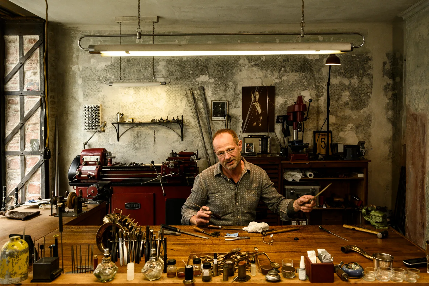 Max Frei at the workbench, gesturing with tools in both hands — Max Frei, saxophone workshop in Icking near Munich, corporate portraits and editorial photography by Janina Laszlo