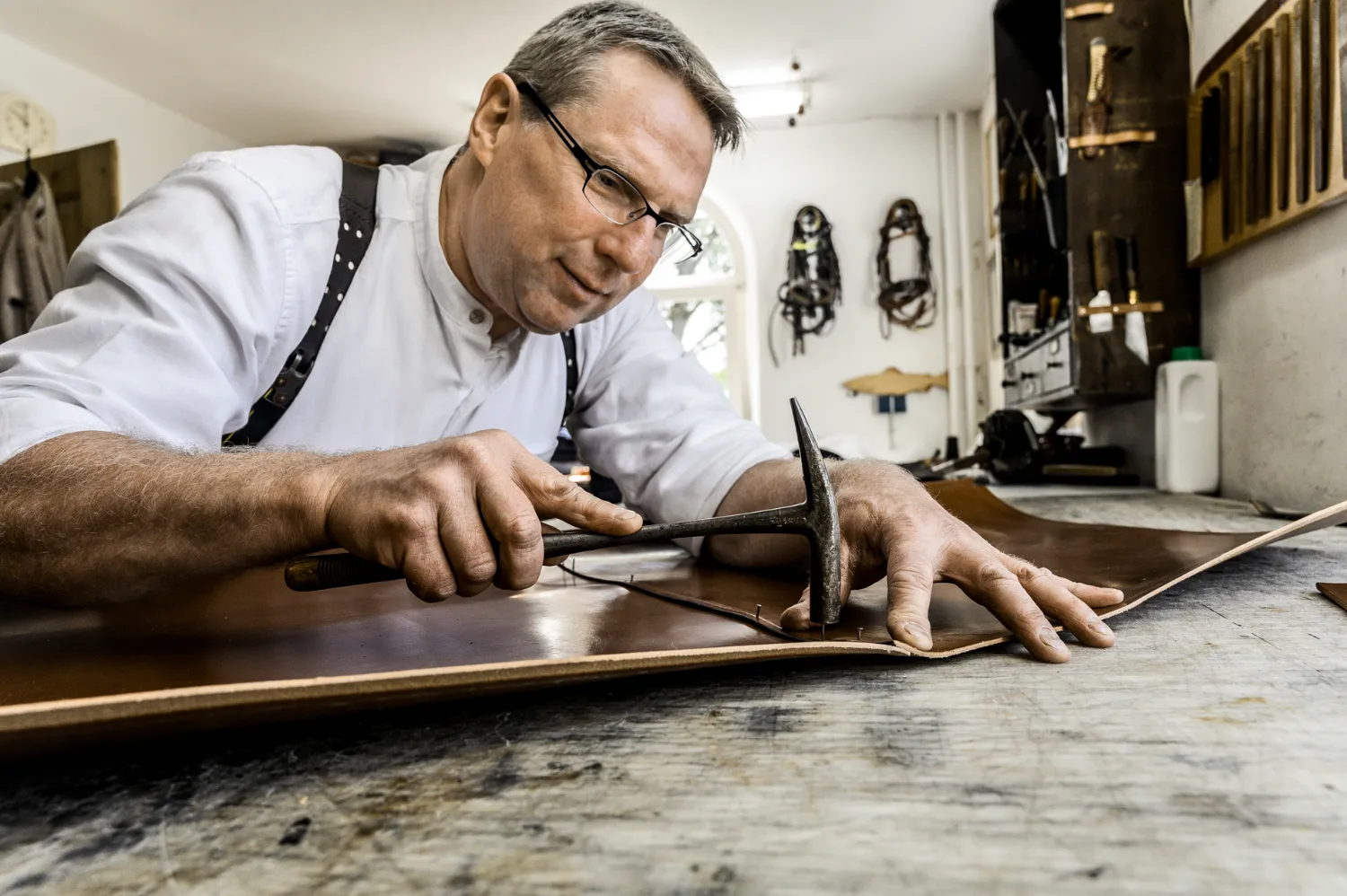 Saddler Michael Ruoff tacking leather to his workbench with a hammer — Michael Ruoff, master saddler, editorial portrait and craftsmanship photography by Janina Laszlo