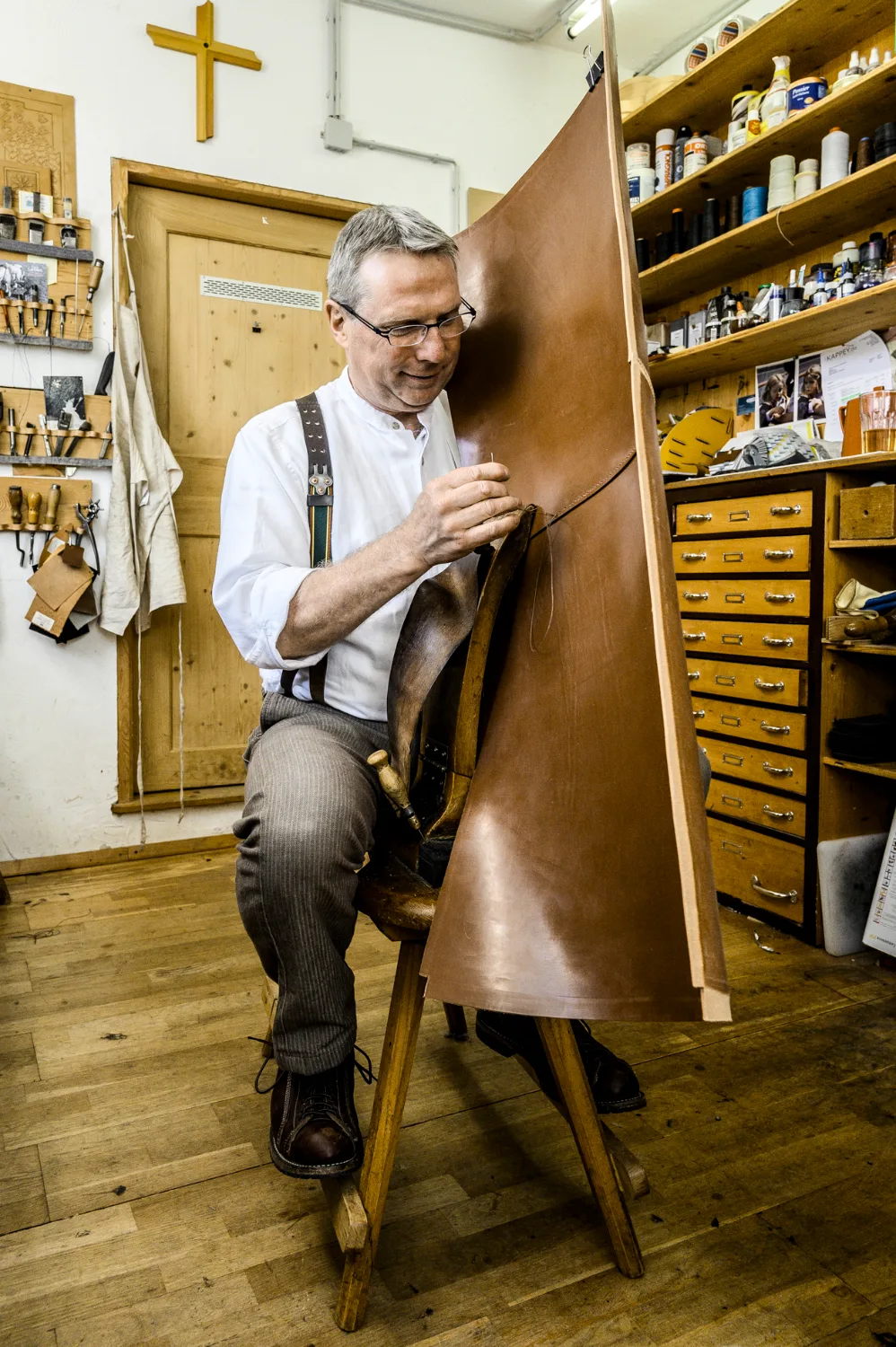 Michael Ruoff sitting on his stitching horse, sewing a large leather piece by hand in his workshop — Michael Ruoff, master saddler, editorial portrait and craftsmanship photography by Janina Laszlo