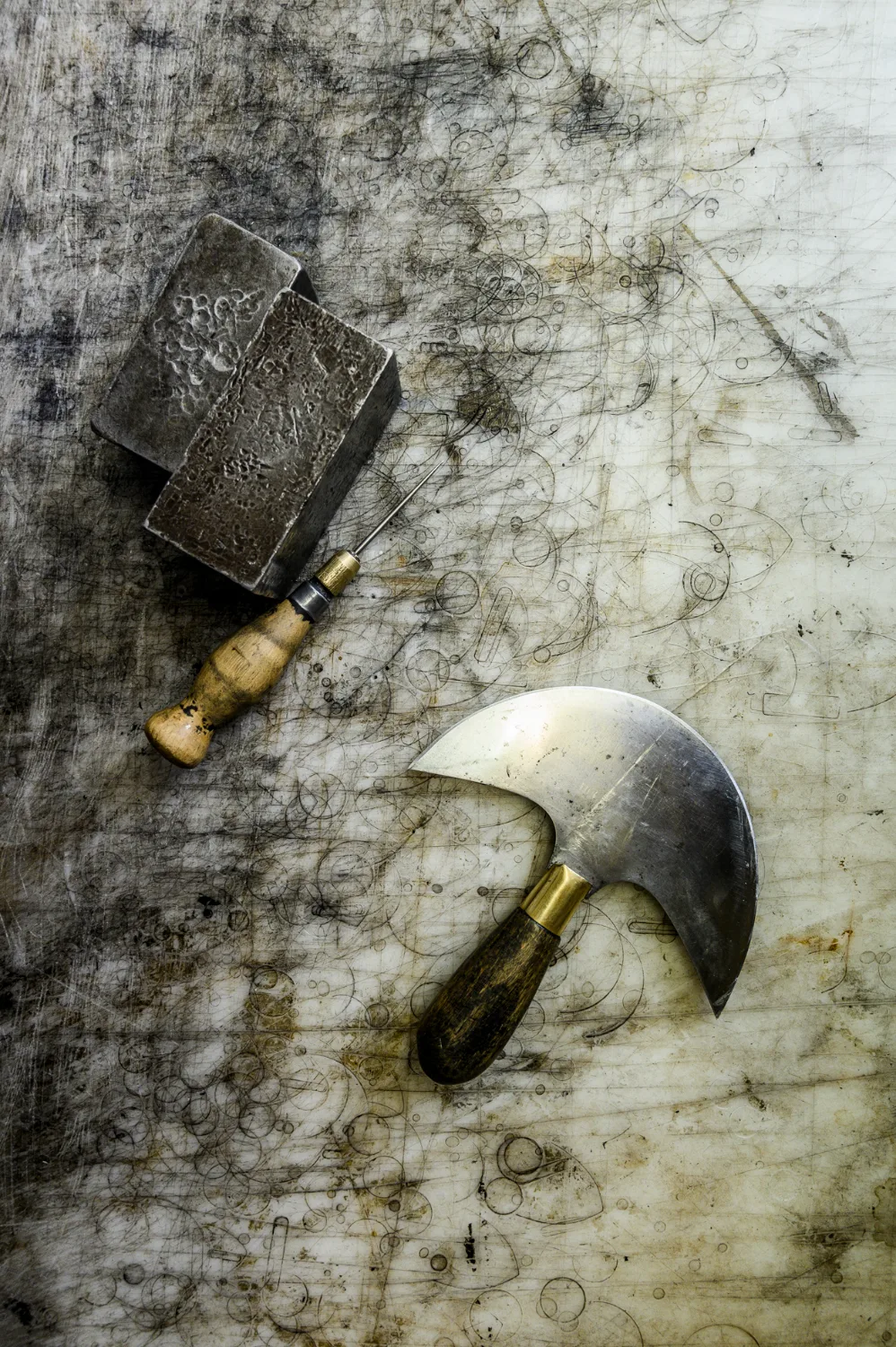 Head knife and awl with lead weights on a worn cutting board — Michael Ruoff, master saddler, editorial portrait and craftsmanship photography by Janina Laszlo