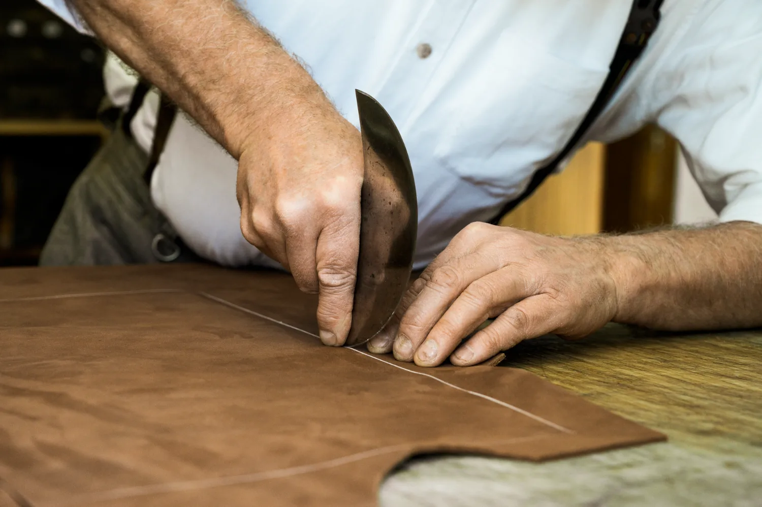 Hands cutting leather along a line with a curved head knife — Michael Ruoff, master saddler, editorial portrait and craftsmanship photography by Janina Laszlo