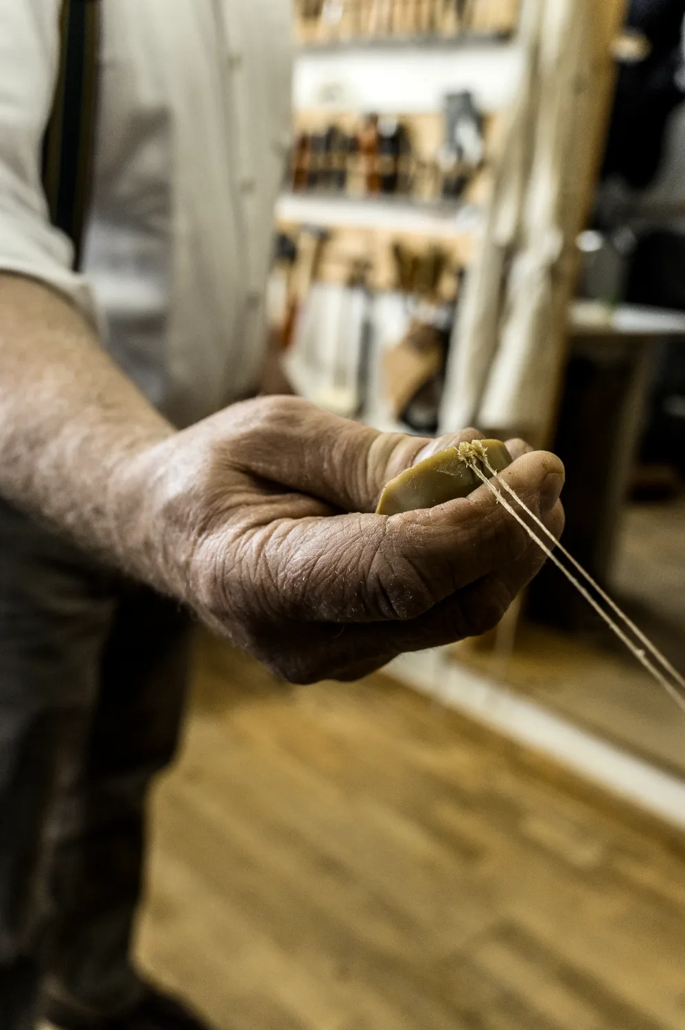 Hand pulling linen thread through a block of beeswax — Michael Ruoff, master saddler, editorial portrait and craftsmanship photography by Janina Laszlo