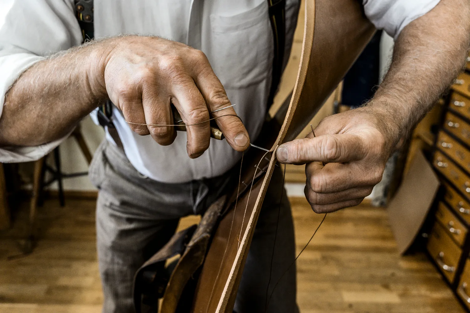 Hands hand-stitching a leather strap with awl and needle — Michael Ruoff, master saddler, editorial portrait and craftsmanship photography by Janina Laszlo