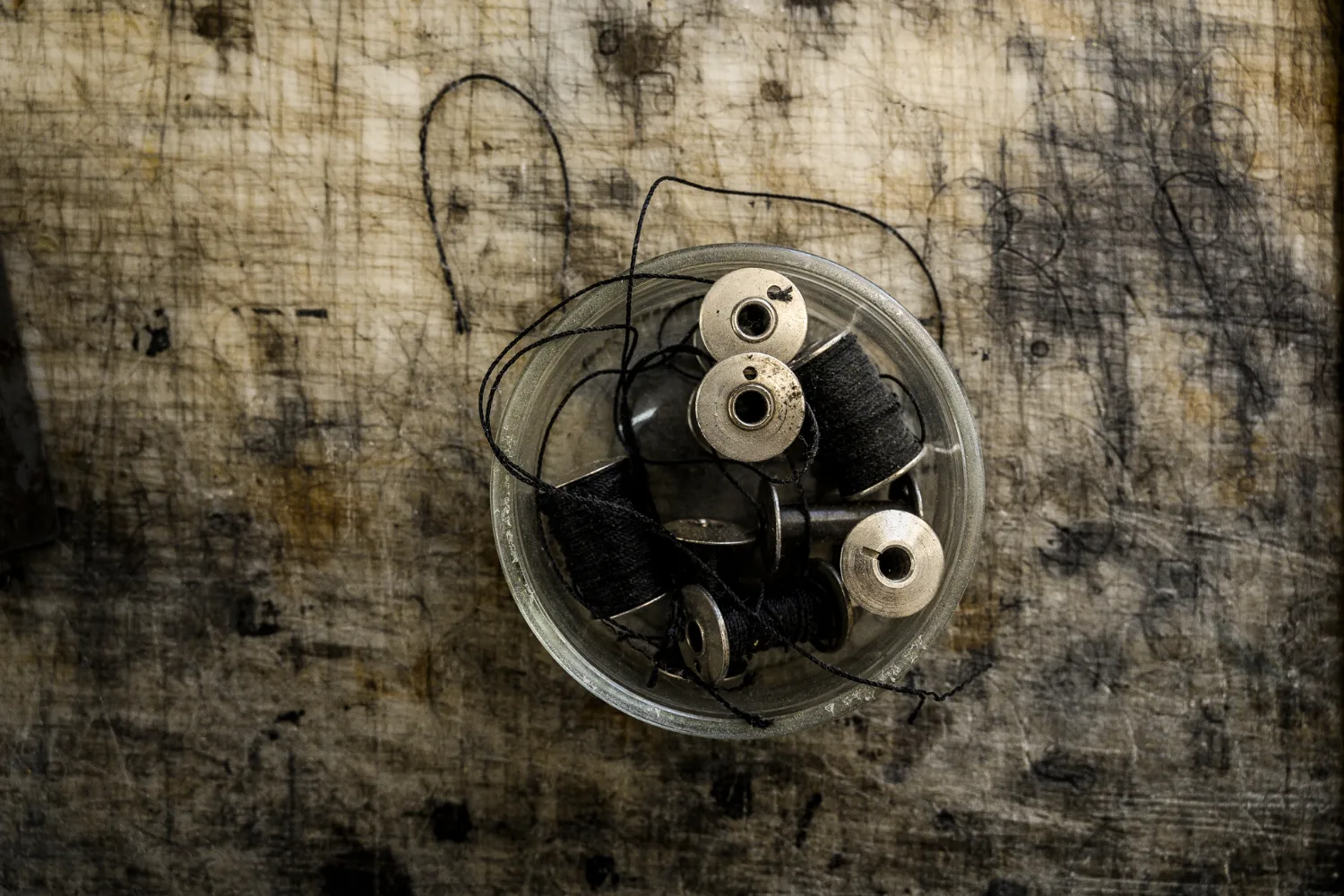 Glass jar with bobbins and black thread on a worn workbench — Michael Ruoff, master saddler, editorial portrait and craftsmanship photography by Janina Laszlo
