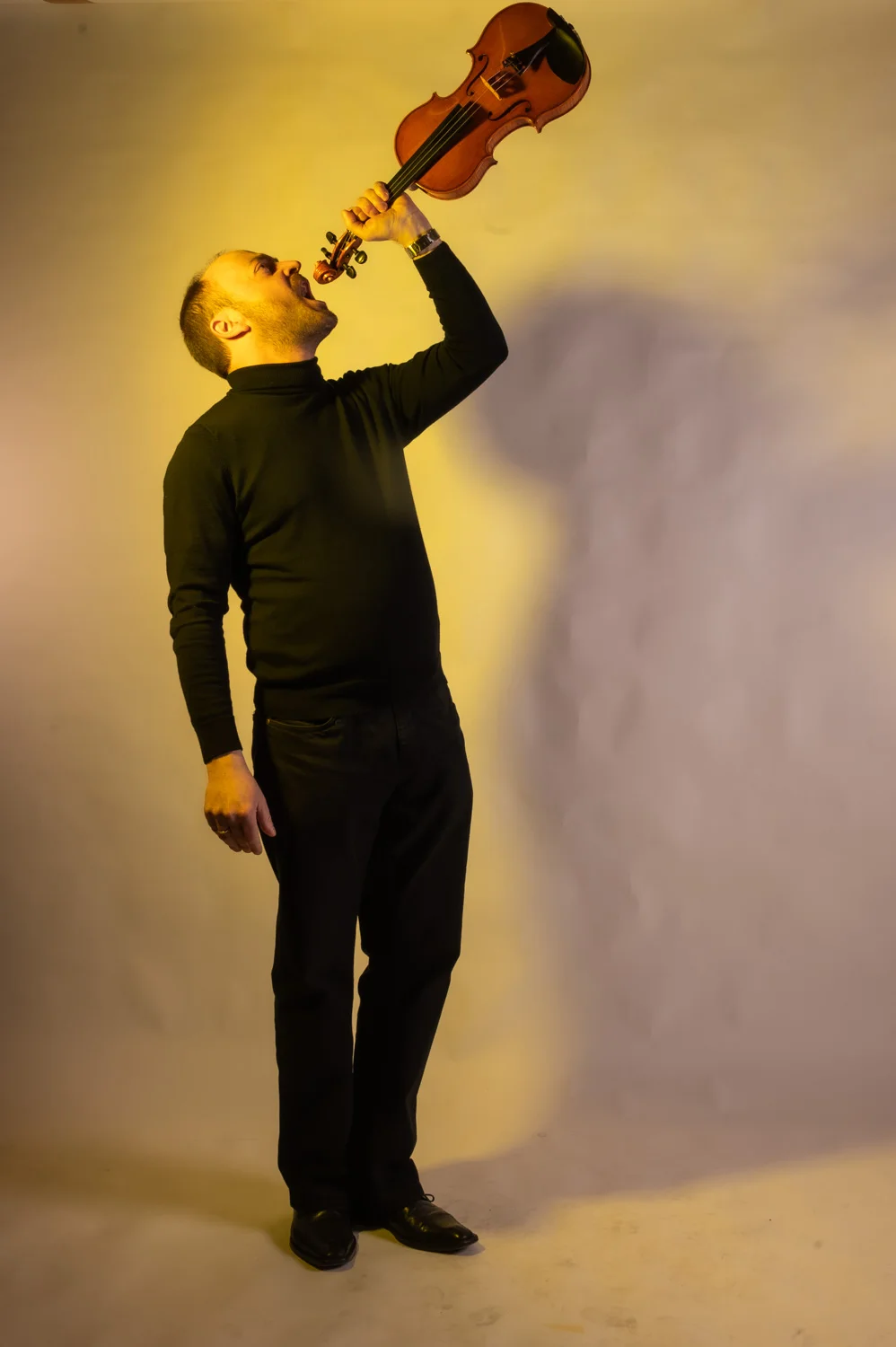 Musician raising his violin high in a playful pose, warm yellow backdrop — Münchner Symphoniker, musician portrait photography by Janina Laszlo, Munich
